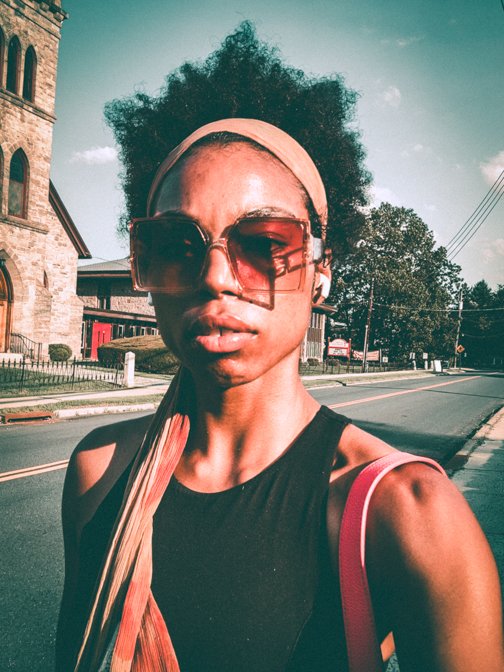 Confident woman in oversized sunglasses and headscarf walking on a sunny day, photographed outside a historic church.