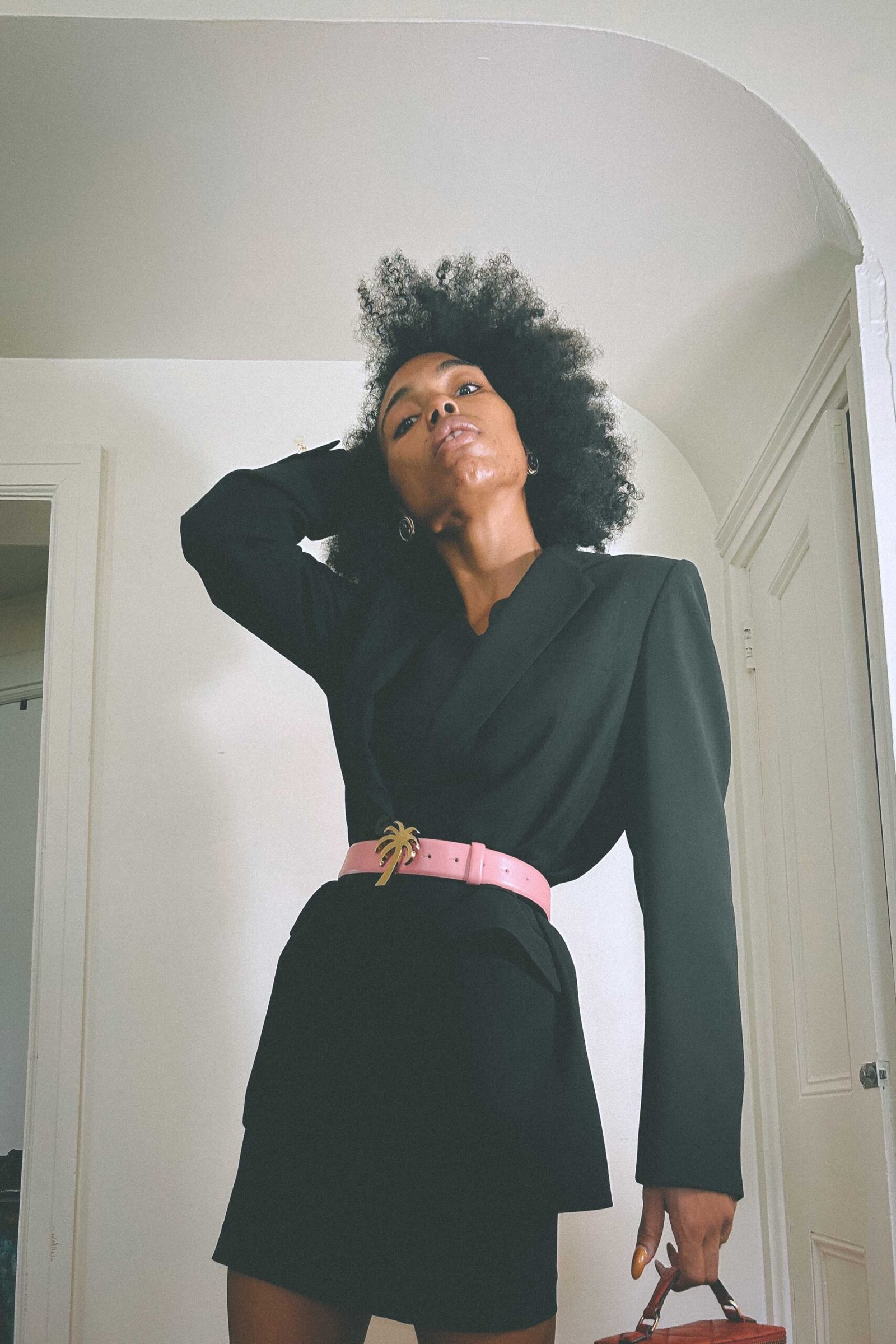 Low angle portrait of 80s-inspired outfit featuring a cinched black blazer and designer belt statement.