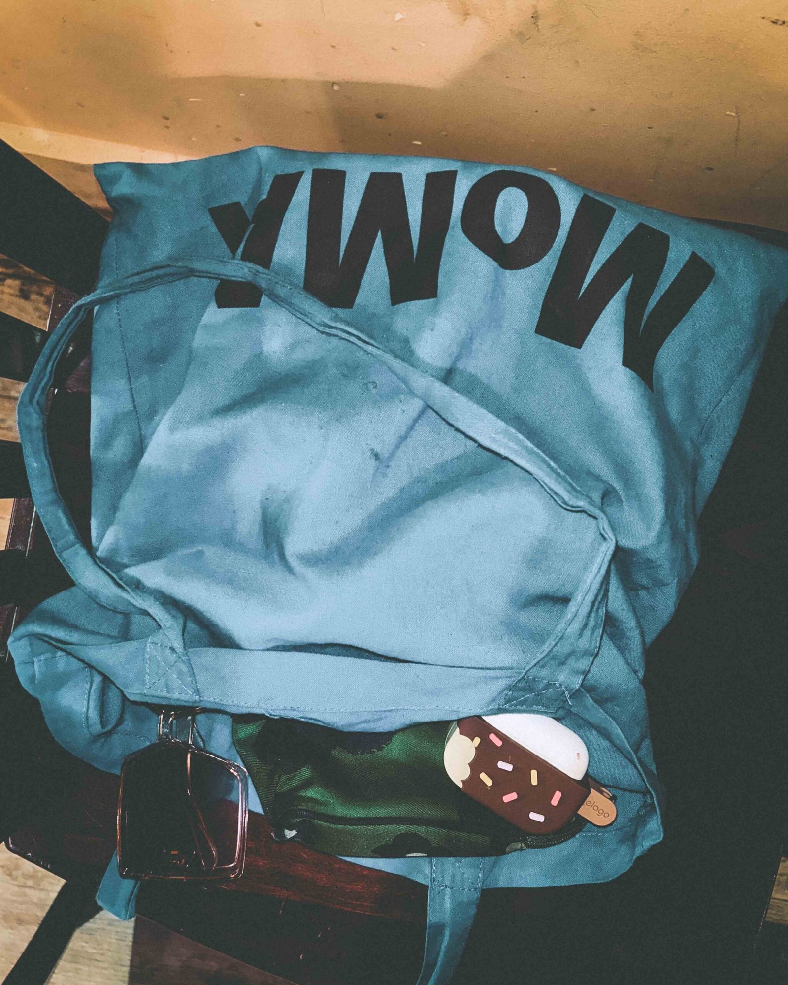 Blue MoMA tote bag with sunglasses and ice cream keychain resting on a wooden chair.