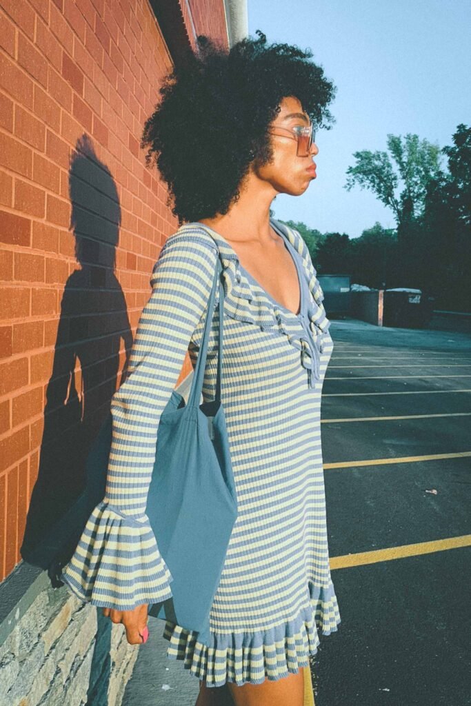 Side profile of woman in blue and yellow striped ruffle dress with flared sleeves carrying blue tote bag.