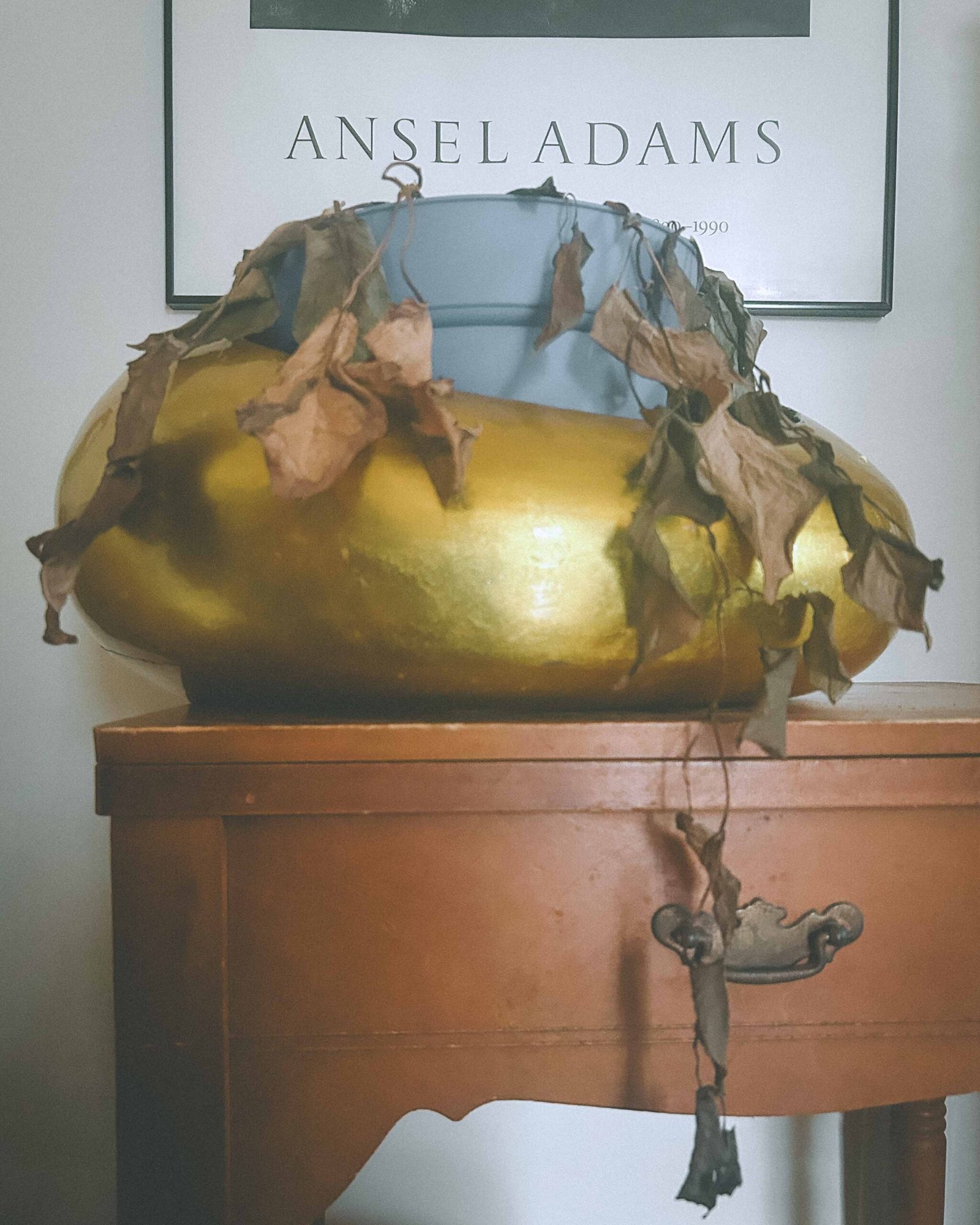 Thrifted gold vase with dried foliage on a wooden side table, styled under an Ansel Adams art print in a boho luxe apartment.
