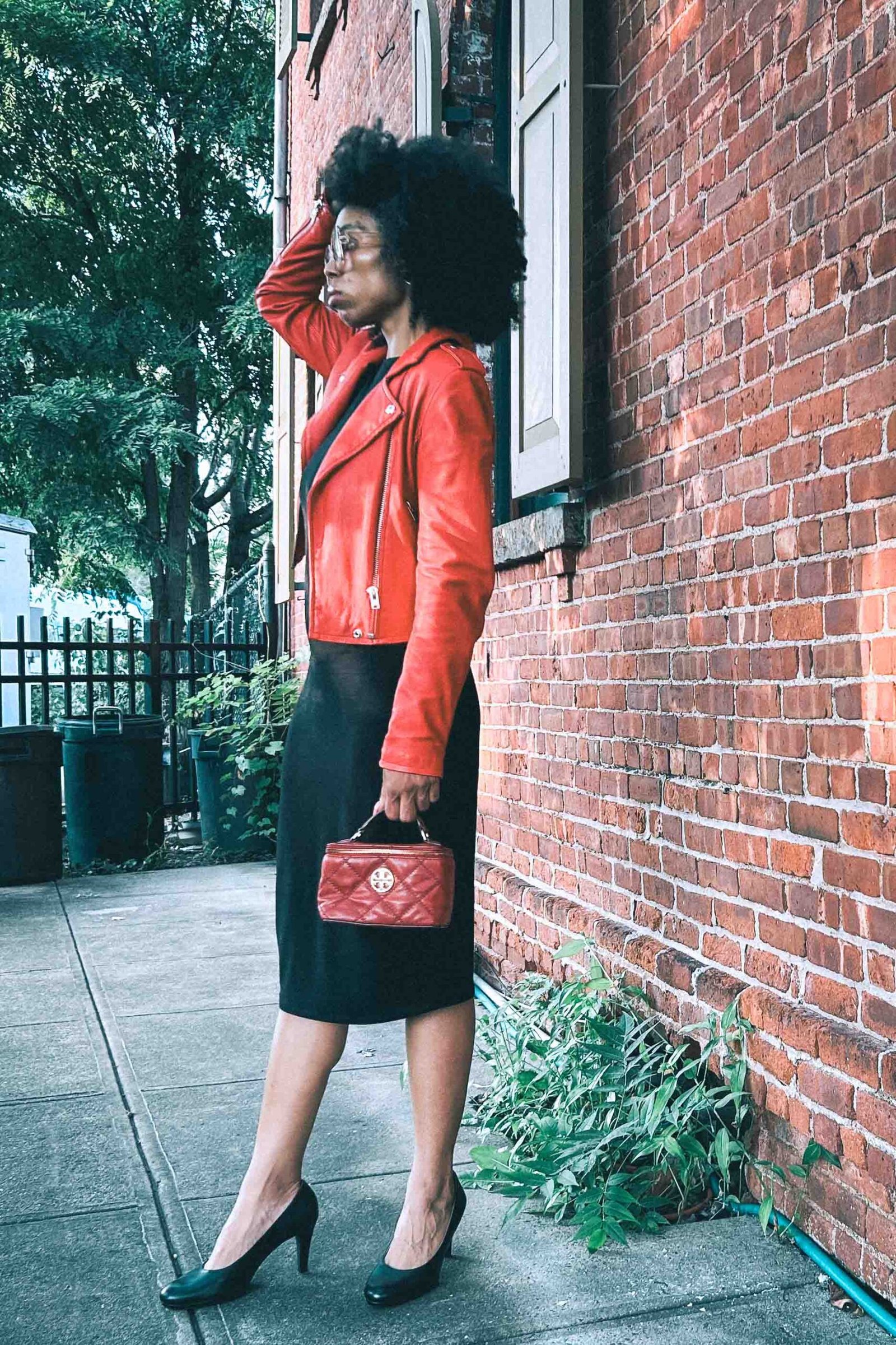 Red leather moto jacket styled with black dress and quilted Tory Burch bag, bold city street style fashion look.