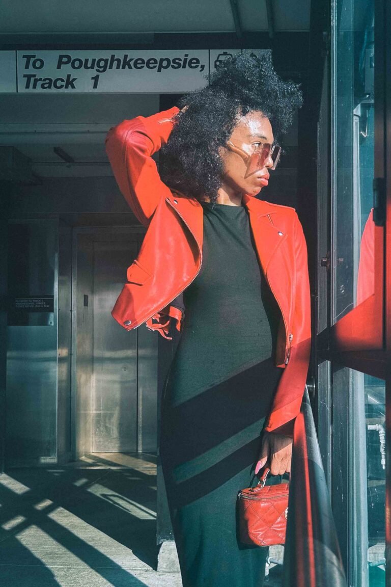 Woman at train station in red leather moto jacket, black dress, and red Tory Burch quilted handbag.