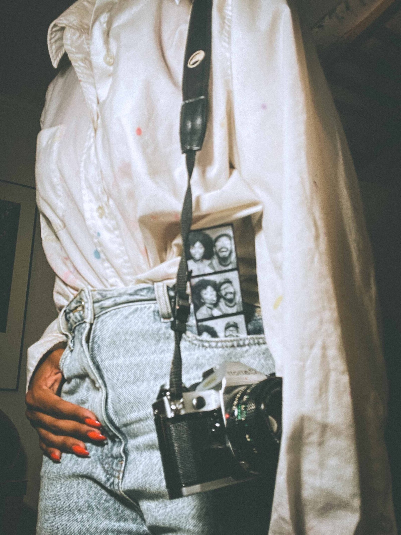 Woman wearing a vintage white shirt and high-waisted jeans with a Canon film camera and black-and-white photo strip in pocket.