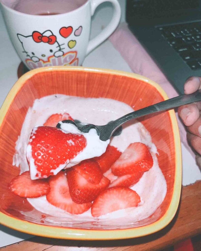 A bowl of strawberries and yogurt with a cozy mug beside a laptop — everyday rituals that nurture creativity and balance during burnout recovery.
