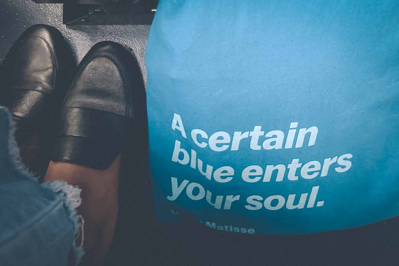 Black leather loafers beside a blue Henri Matisse tote bag that reads “A certain blue enters your soul” — minimalist travel and creative living aesthetic.