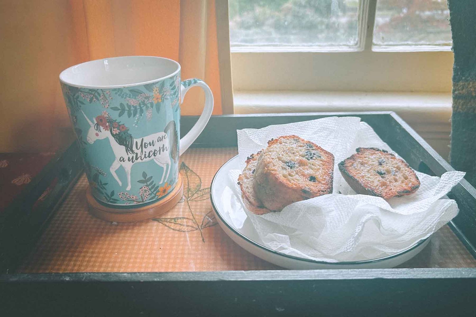 A cozy morning scene in a Hudson Valley apartment — a whimsical unicorn mug and toasted bread on a tray by the window, capturing comfort during a quiet restart.