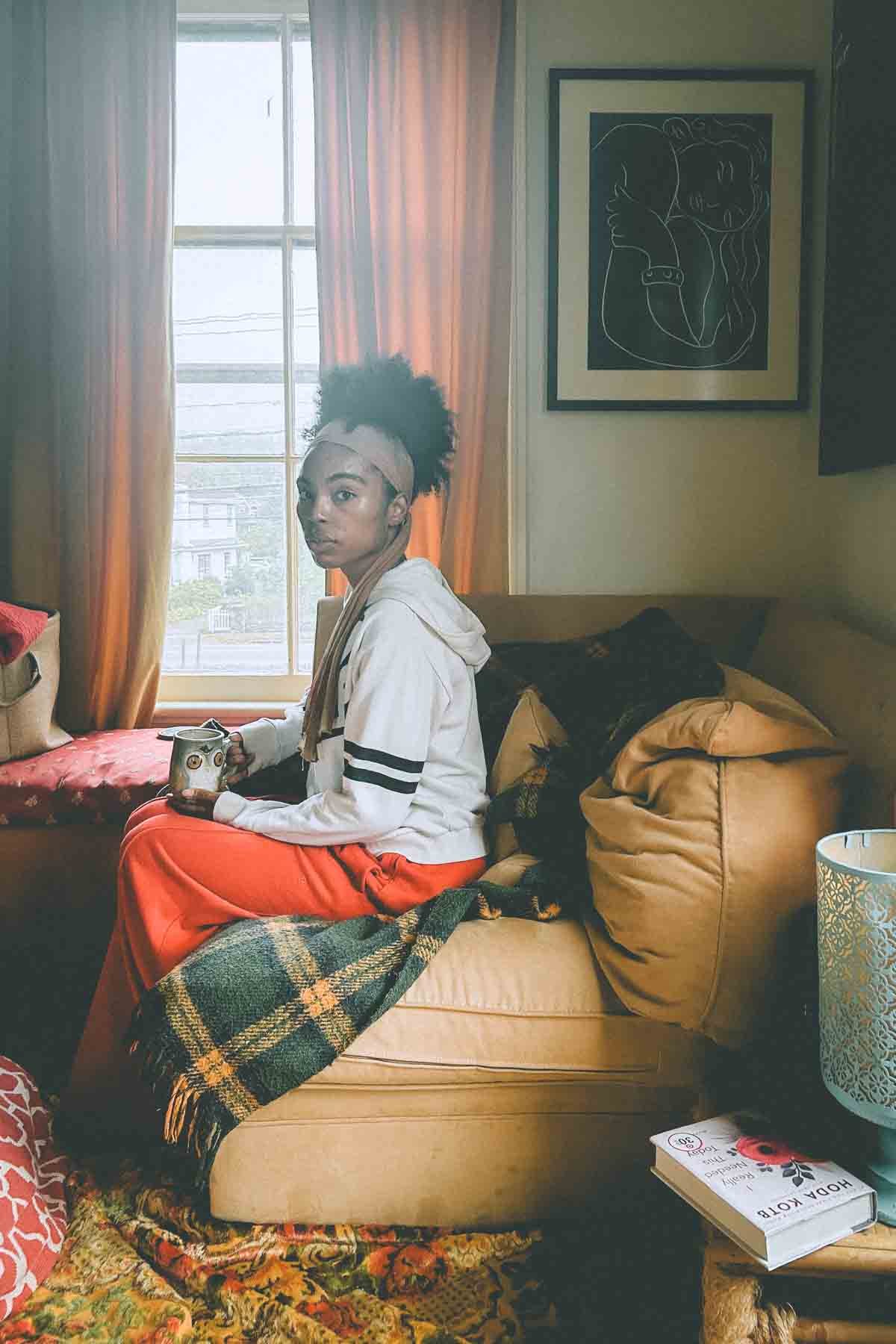 Woman sitting by a window in her cozy Hudson Valley apartment, holding tea — a peaceful moment of reflection and self-care.