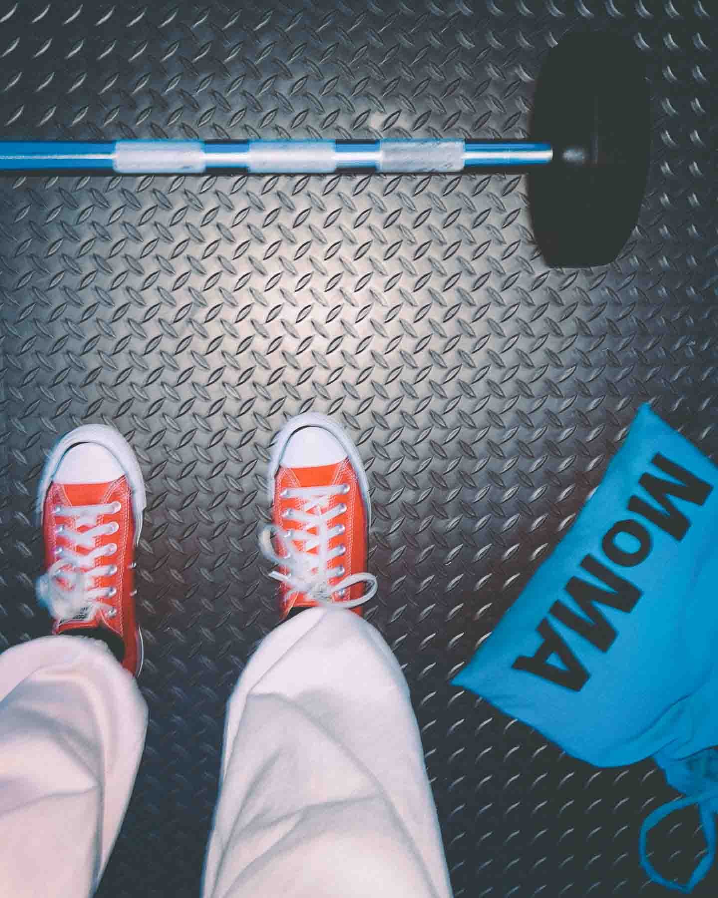 Red sneakers beside a blue MoMA tote and barbell on a textured gym floor — documenting discipline during the process of starting over after burnout.