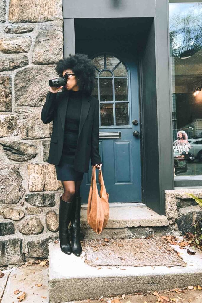 Bohemian fashion blogger in a black and navy outfit with a tailored blazer, and knee-high boots sipping coffee on a fall afternoon in New York.