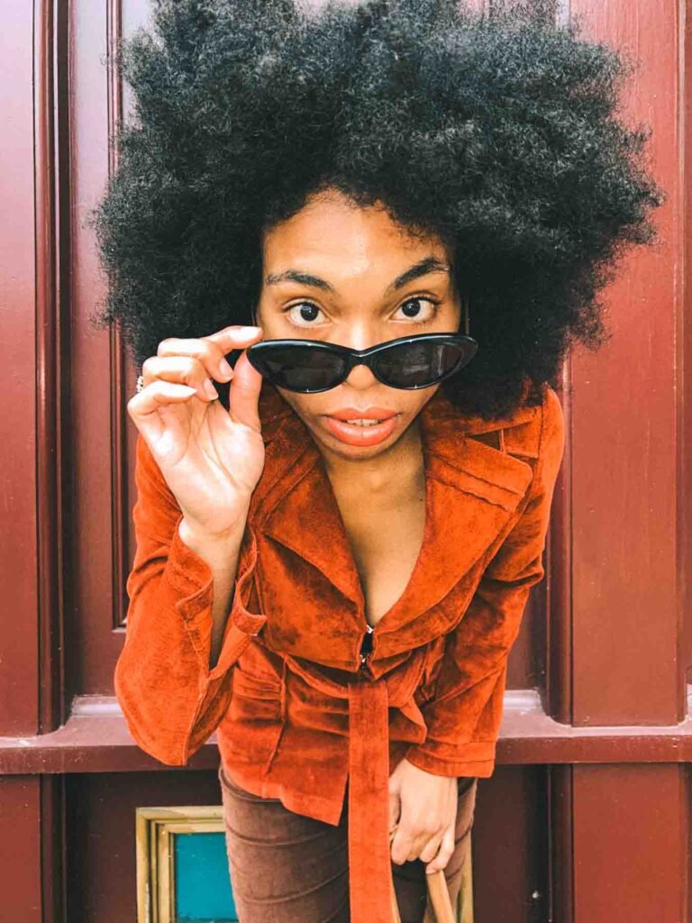 Bohemian style blogger in a rust suede jacket lifting cat-eye sunglasses, fall fashion portrait for Inside My Closet wardrobe series.