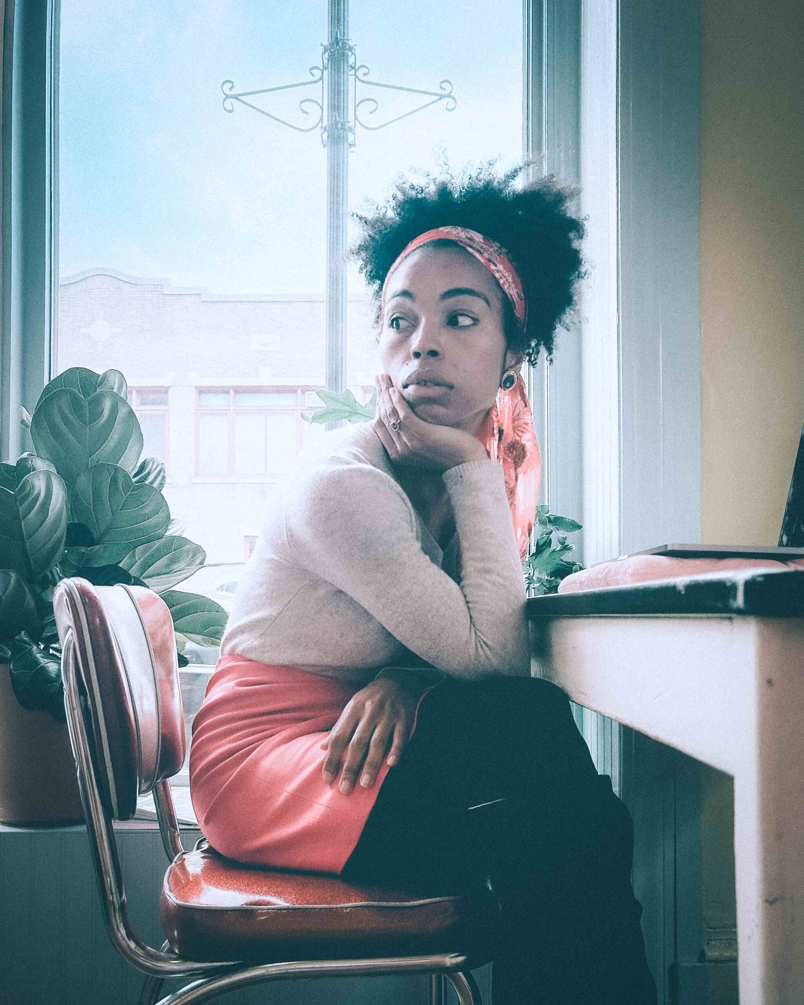 Cinematic portrait of a woman sitting in a cozy coffee shop by a window, expressing quiet reflection during the holiday season.