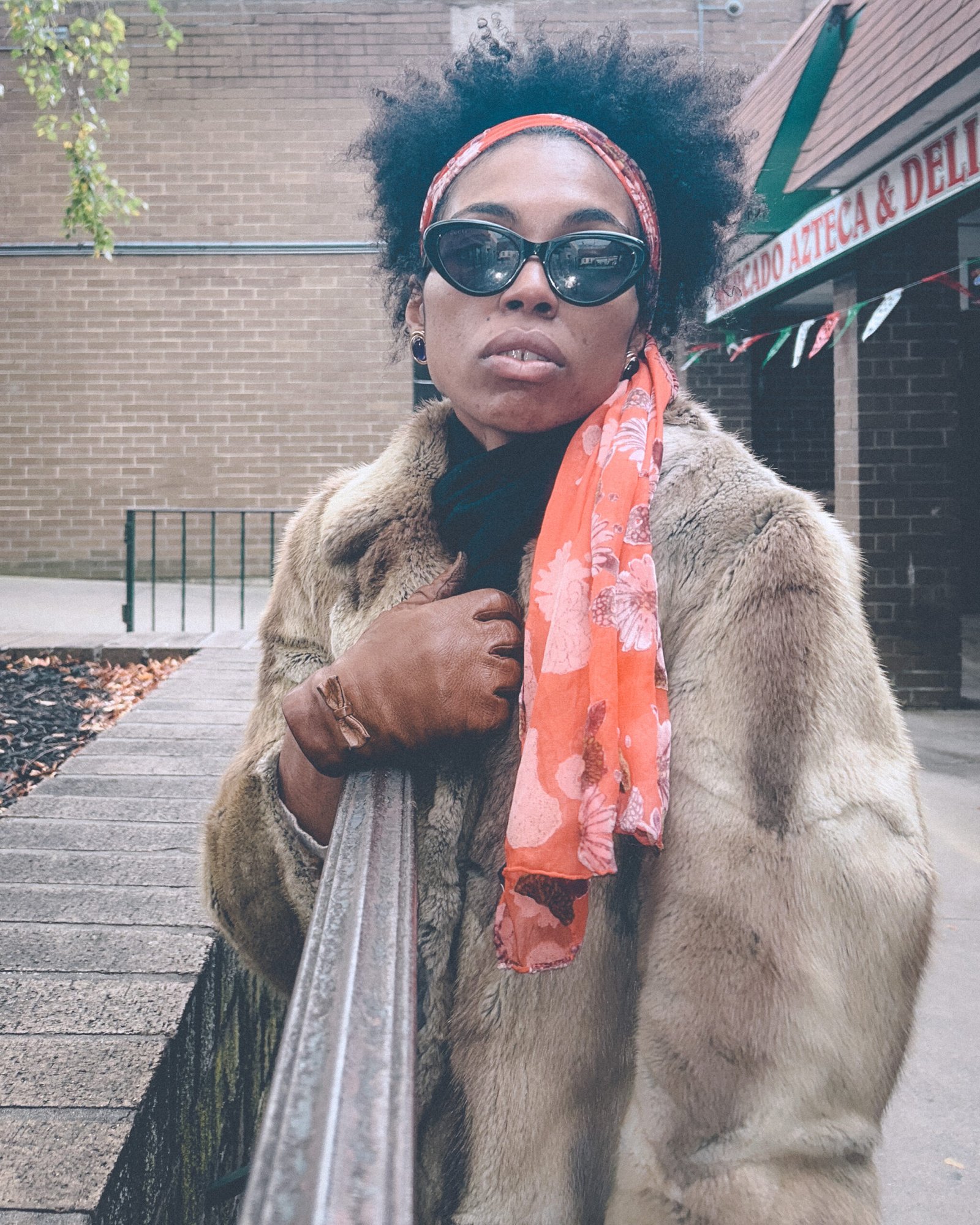 Bohemian fashion portrait of a woman in a vintage fur coat and orange scarf standing outside a deli on a cold November day, capturing a raw winter mood.