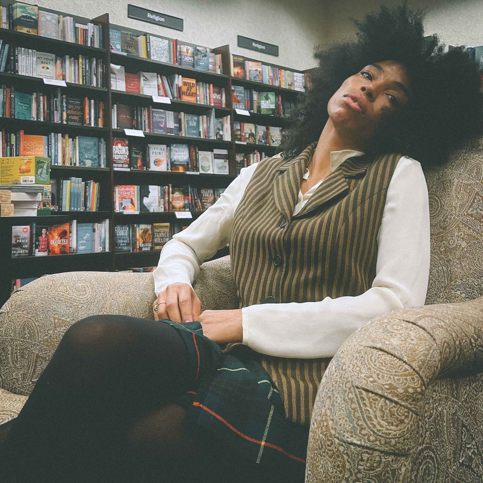 Bohemian blogger in a striped vest and skirt sitting in a bookstore lounge chair, reflecting quietly during the winter blues season.