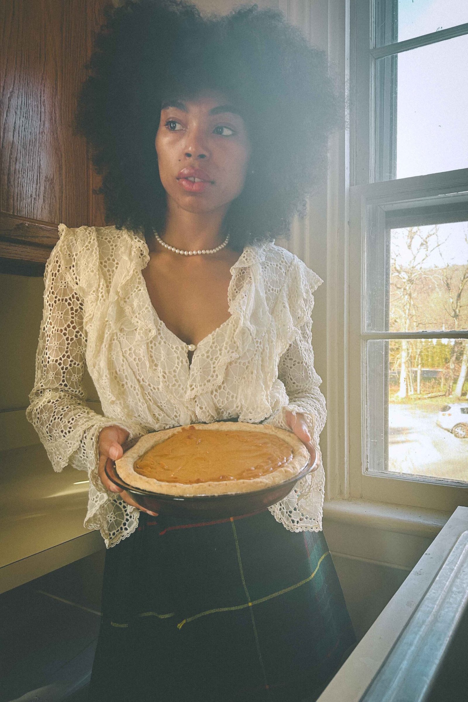 Woman in lace blouse holding a homemade sweet potato pie by a foggy kitchen window, embodying being single during the holidays.