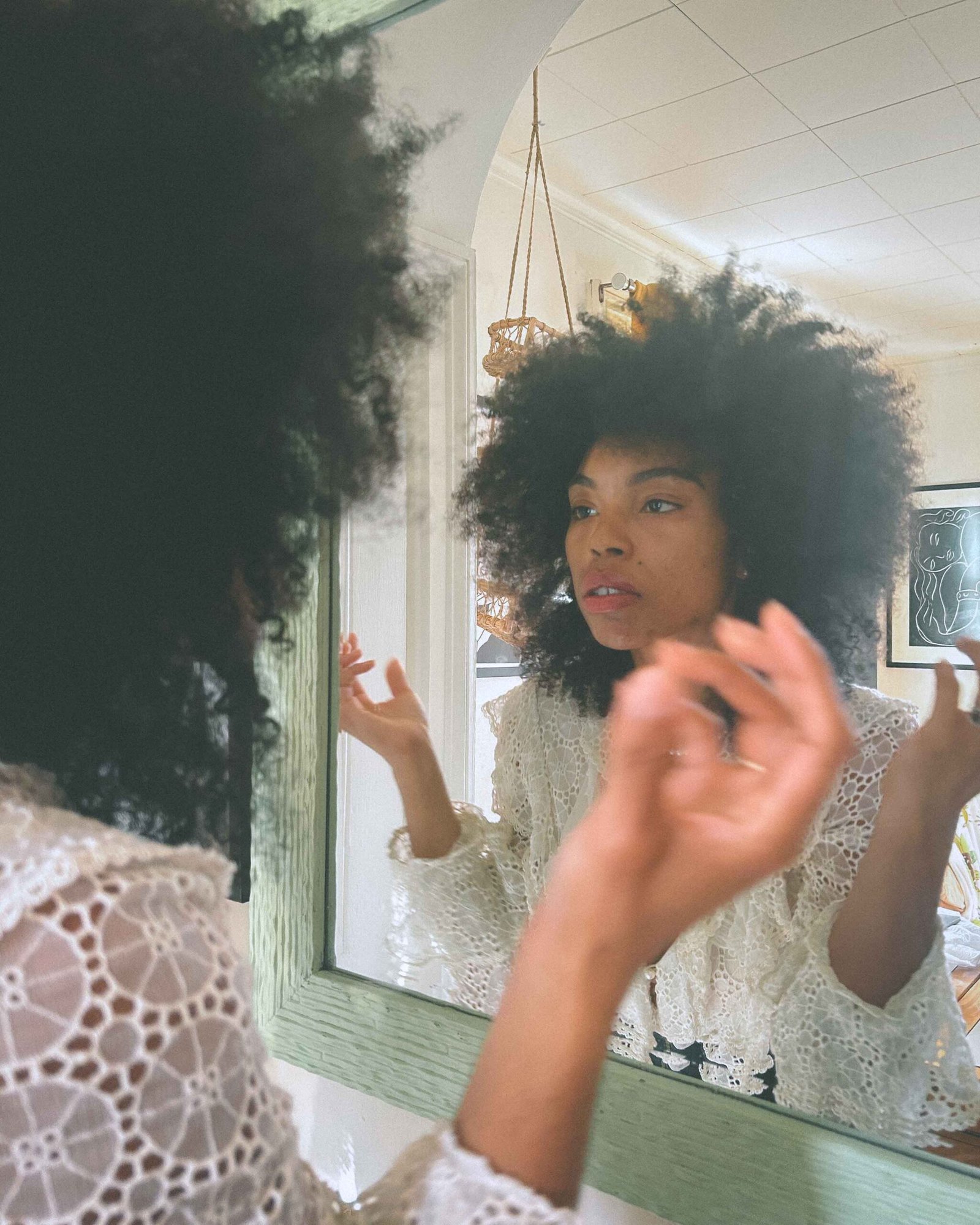 A woman in a vintage lace top adjusts her hair in the mirror, reflecting on loneliness and self-softening while getting ready for Thanksgiving as a single woman during the holidays.
