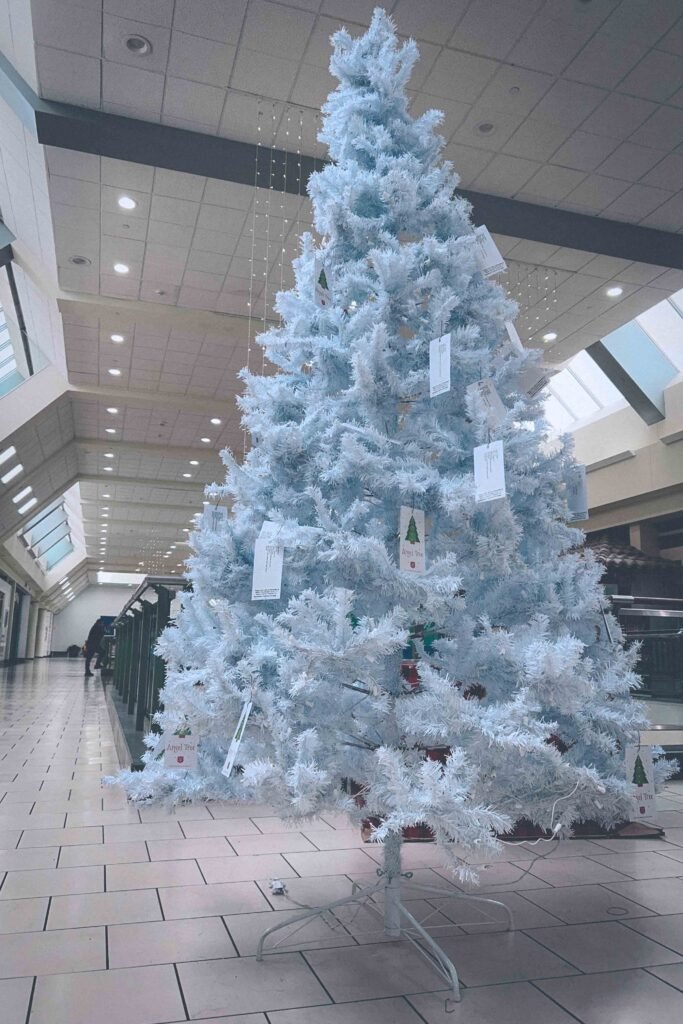 Large white artificial Christmas tree in a quiet mall mezzanine, symbolizing early holiday season ambience and winter melancholy.