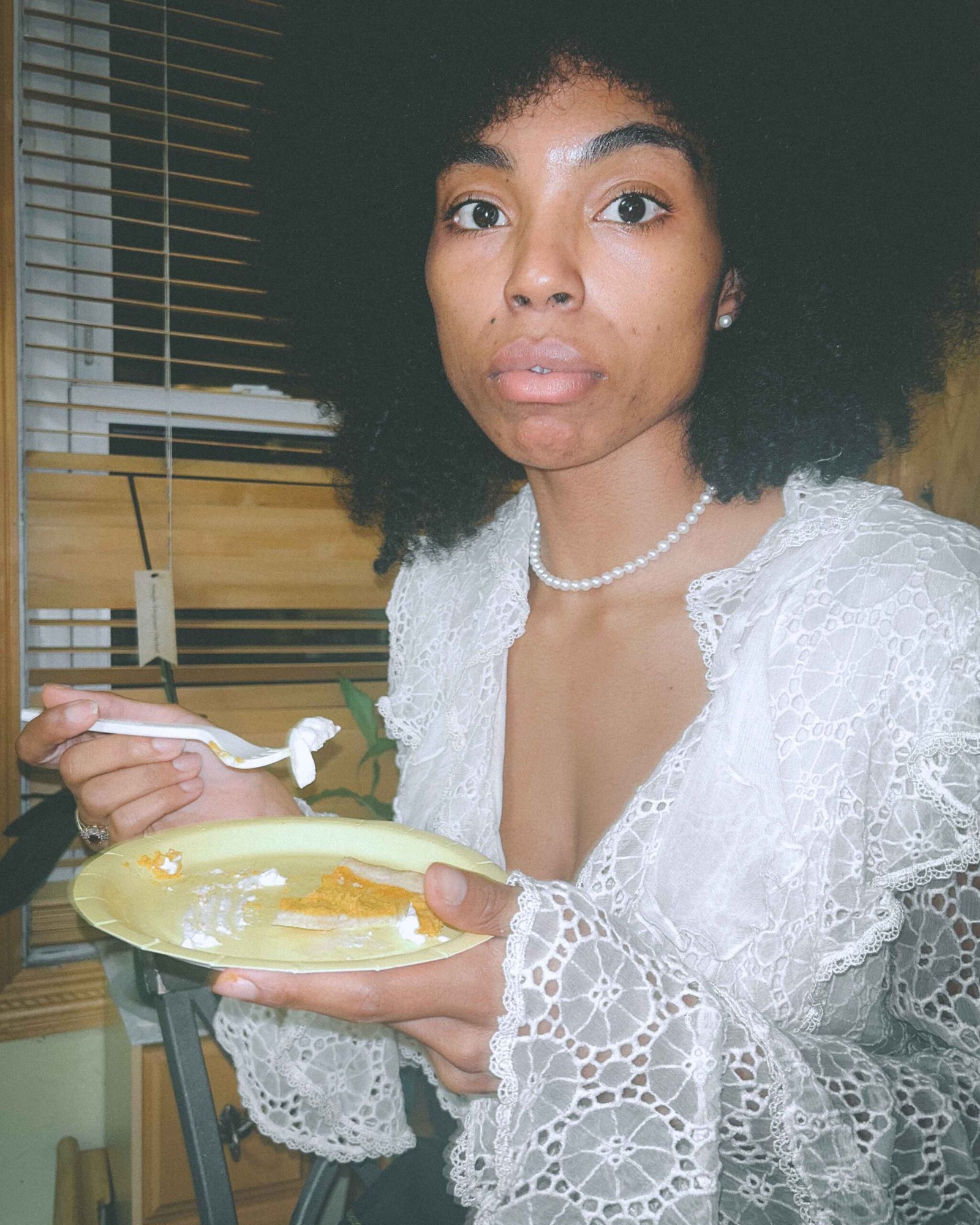 A woman in a white lace blouse eats sweet potato pie with whipped cream in a dimly lit kitchen, documenting the intimate moments of being single during the holiday season.