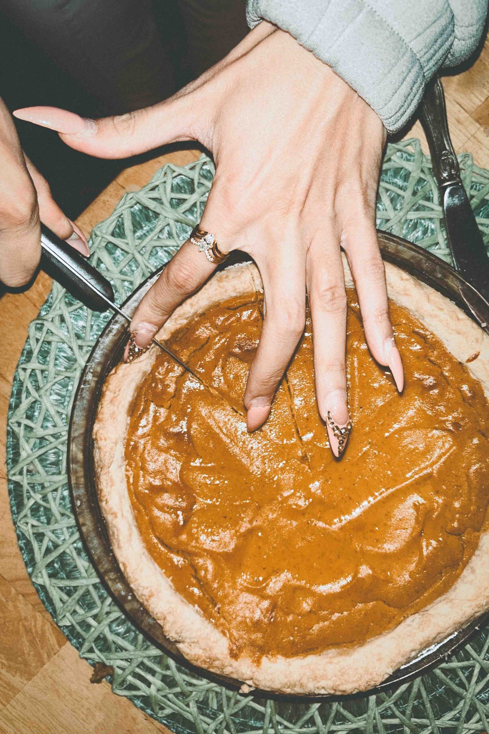 A close-up of hands cutting into a homemade sweet potato pie at Thanksgiving, a symbolic contrast between family togetherness and the experience of being single during the holidays.
