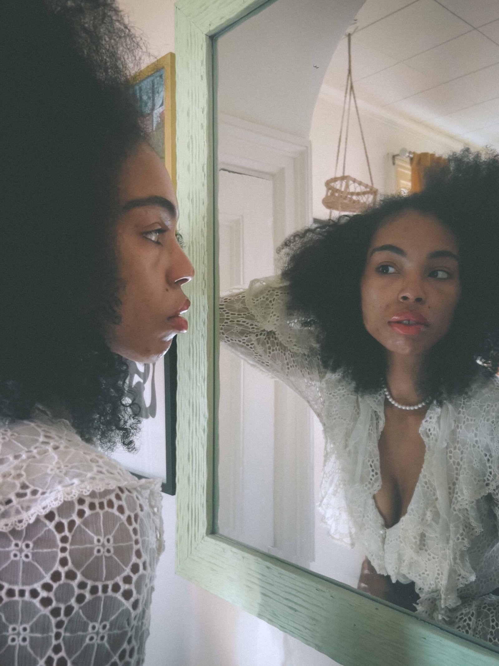 A woman stands before a mirror in a vintage lace top, her reflection capturing the quiet contemplation and loneliness of being single during the holidays.