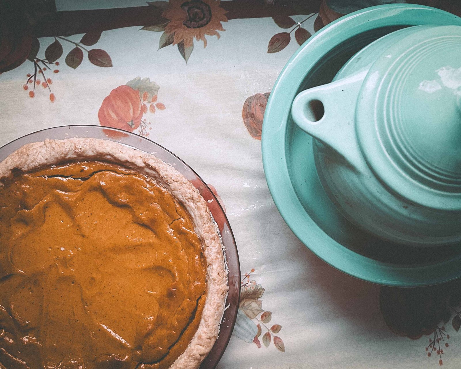 Overhead shot of sweet potato pie next to a vintage turquoise ceramic dish on a fall-themed Thanksgiving tablecloth.
