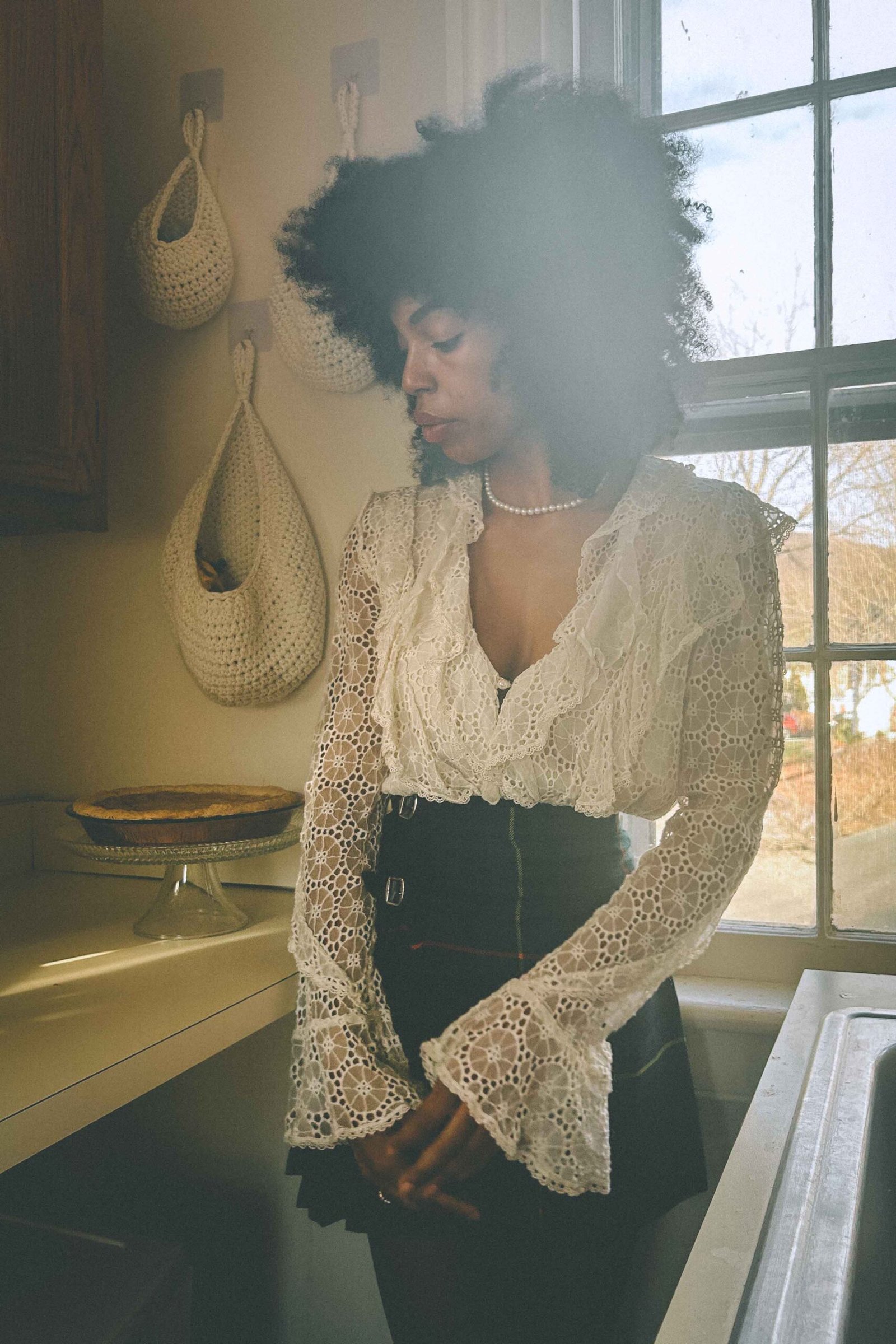 Boho woman standing in a sunlit kitchen beside a sweet potato pie, portraying quiet loneliness during the holiday season.