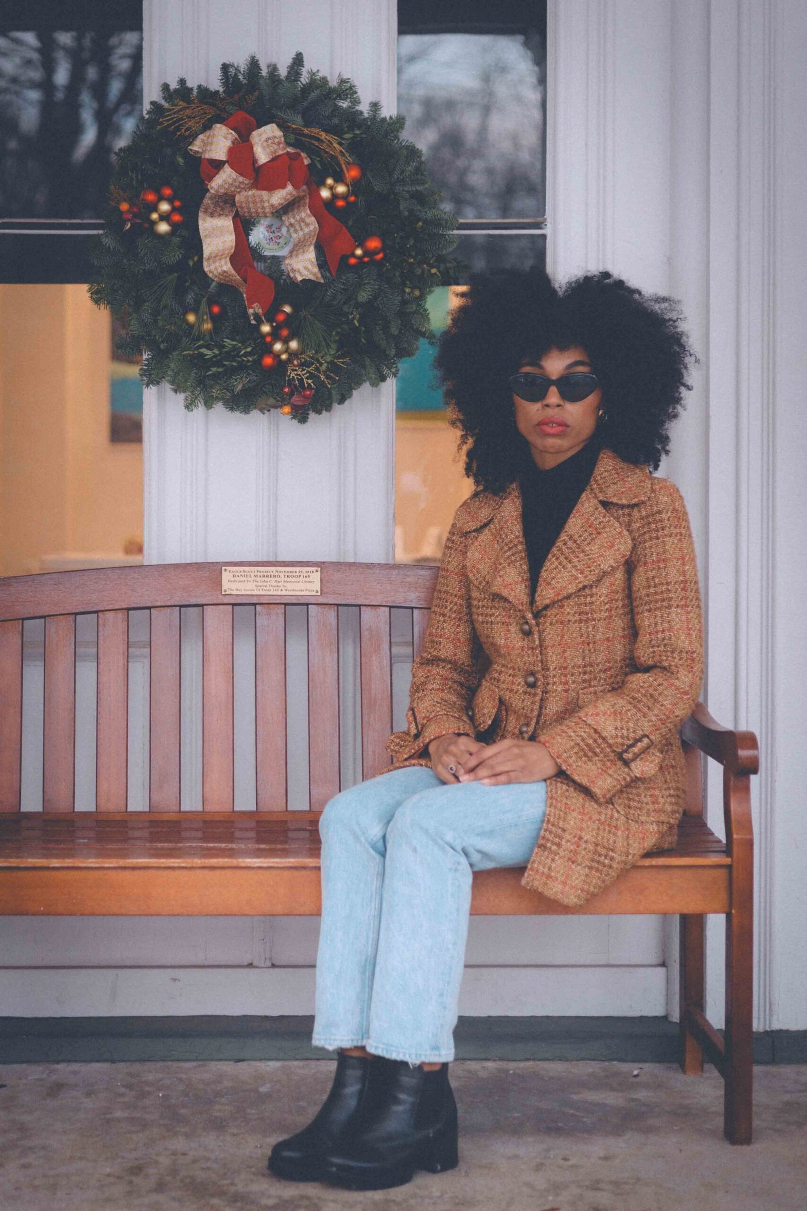 Vintage-inspired wool winter coat worn casually with light-wash jeans and black boots on a snowy porch. 