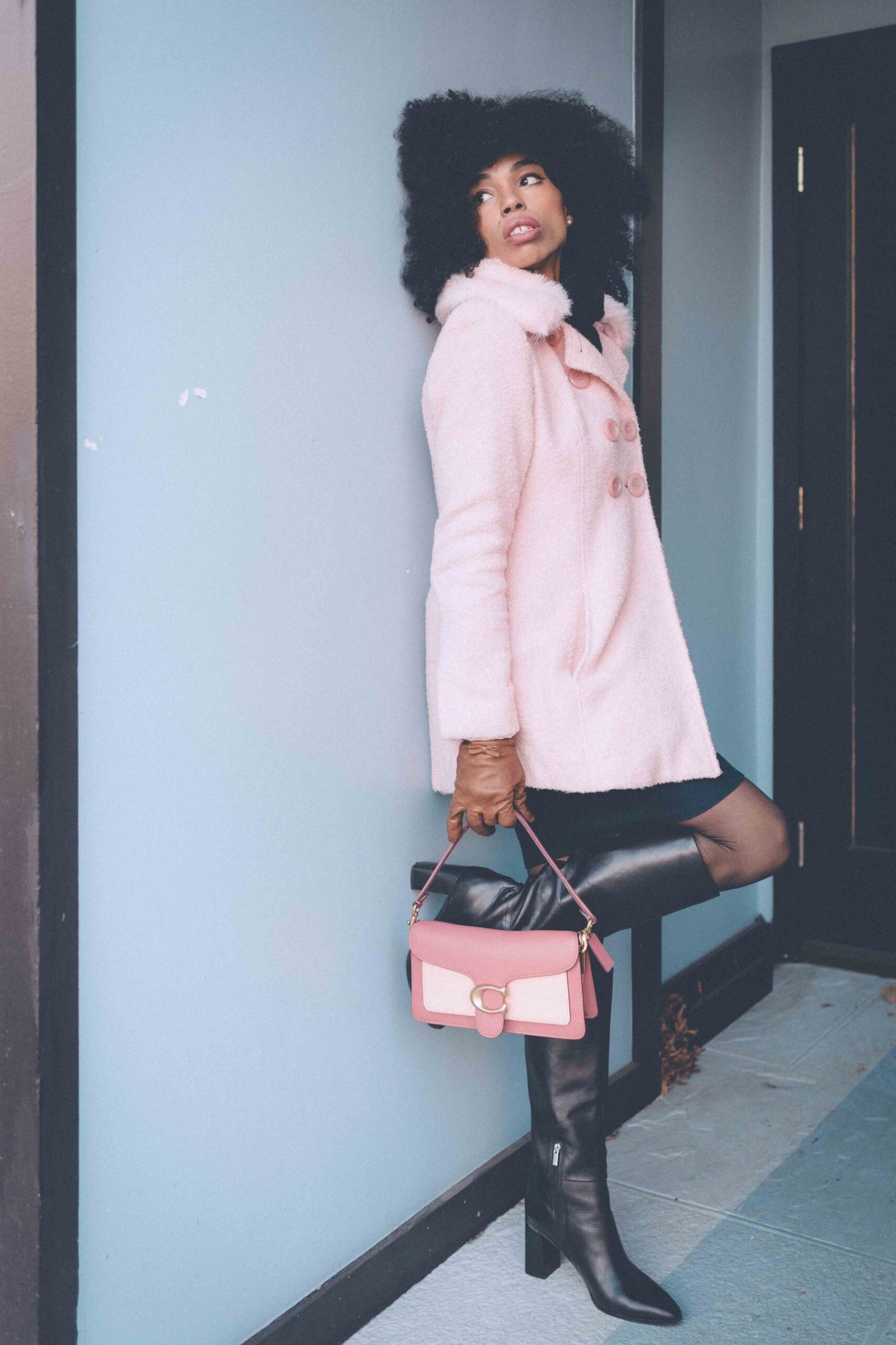 Soft pink winter coat styled with black knee-high boots and a blush leather shoulder bag, photographed outdoors for a boho luxe winter wardrobe.