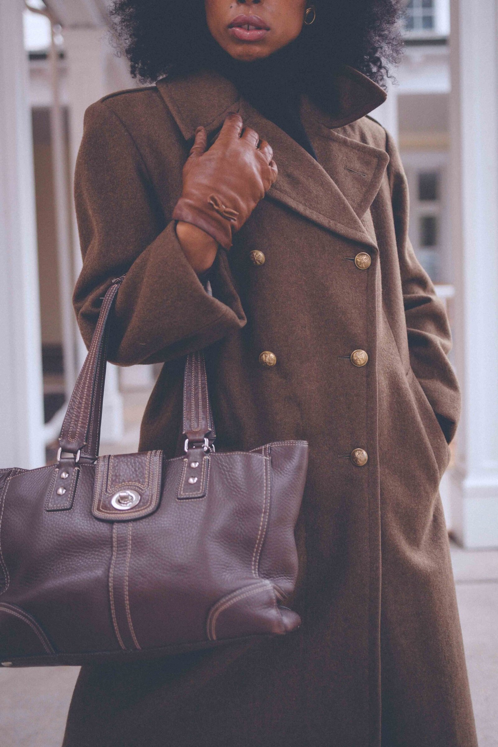 Olive wool statement coat styled with black knee-high boots and a leather tote, photographed under white columns for a classic winter look.