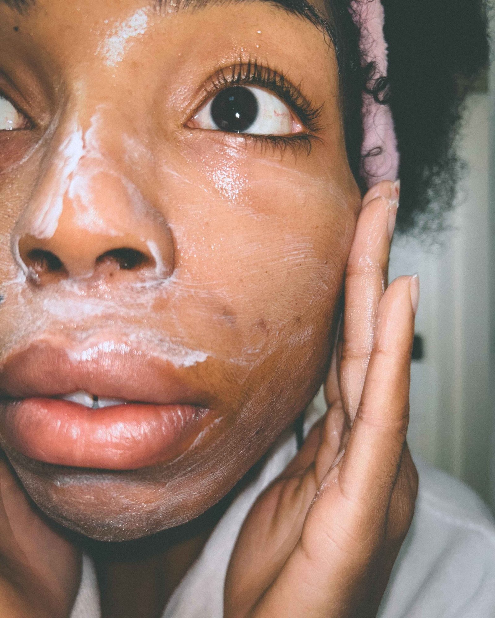 A close-up shot of a bohemian woman applying a gentle moisturizing cream to her face during her winter skincare routine.