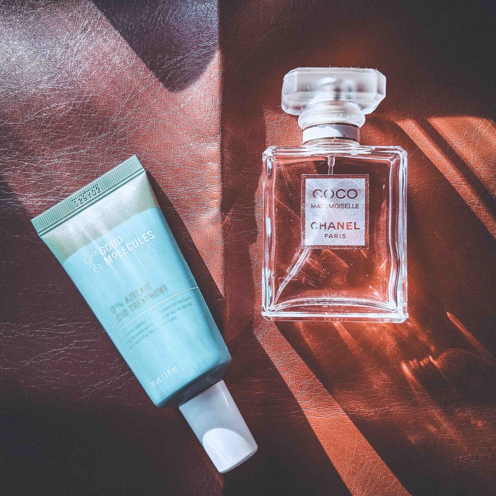 A flatlay of Good Molecules azelaic acid treatment and a Chanel Coco Mademoiselle perfume bottle resting on a textured brown surface, styled for a bohemian beauty routine.