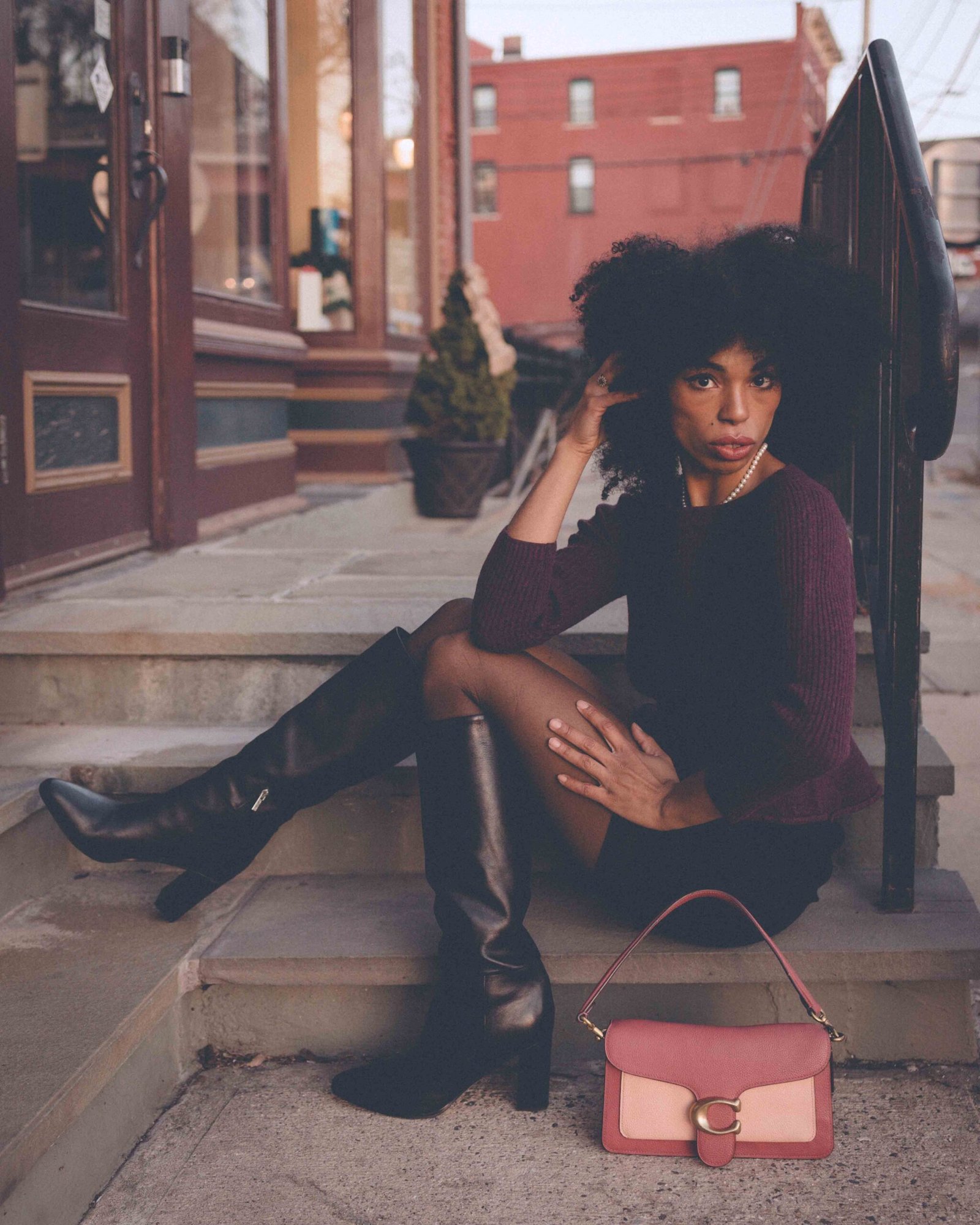 Winter outfit featuring a burgundy sweater, black skirt, sheer tights, knee-high boots, and a structured pink handbag styled for everyday city wear.