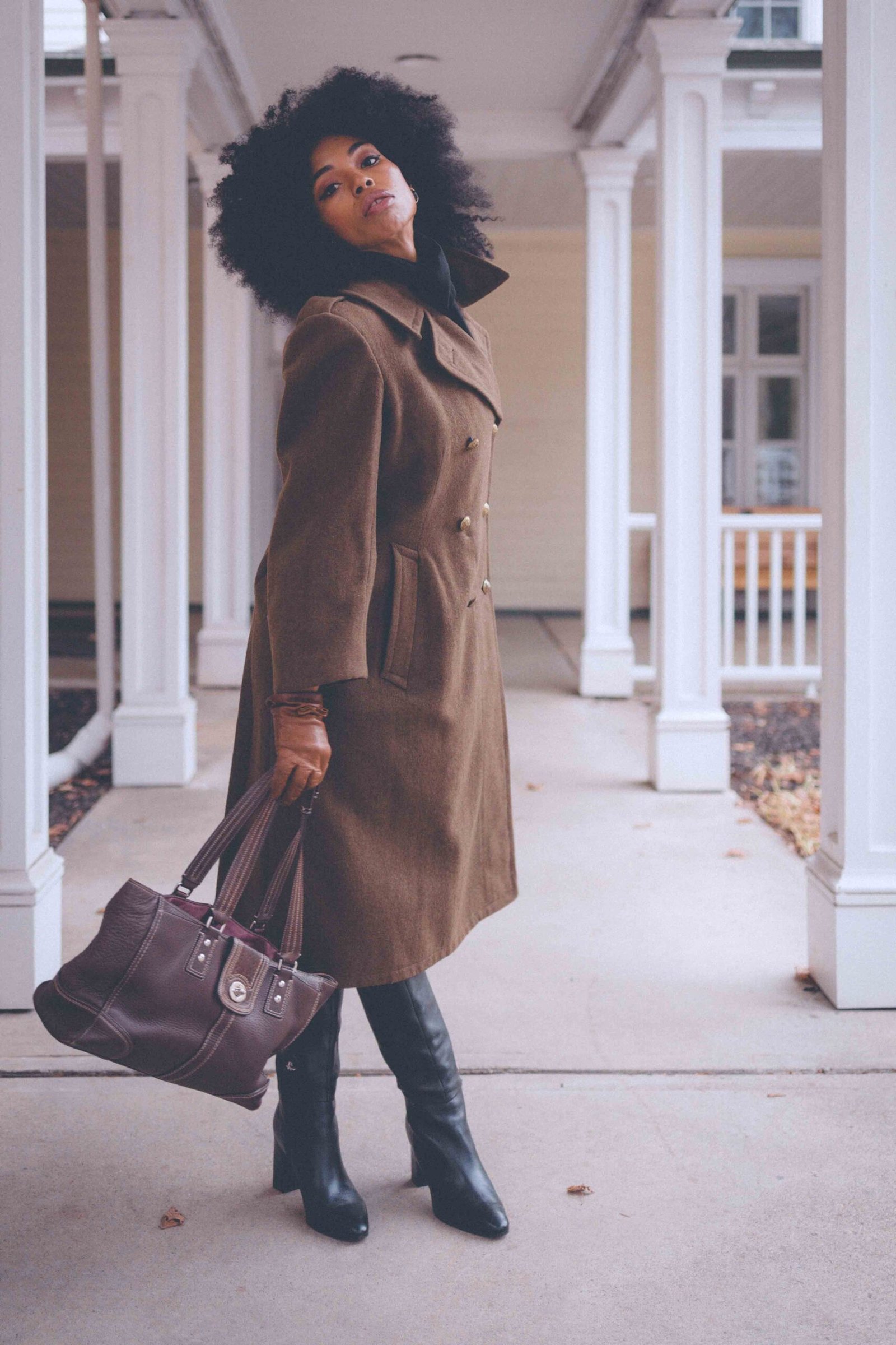 Olive wool statement coat styled with black knee-high boots and a leather tote, photographed under white columns for a classic winter look.