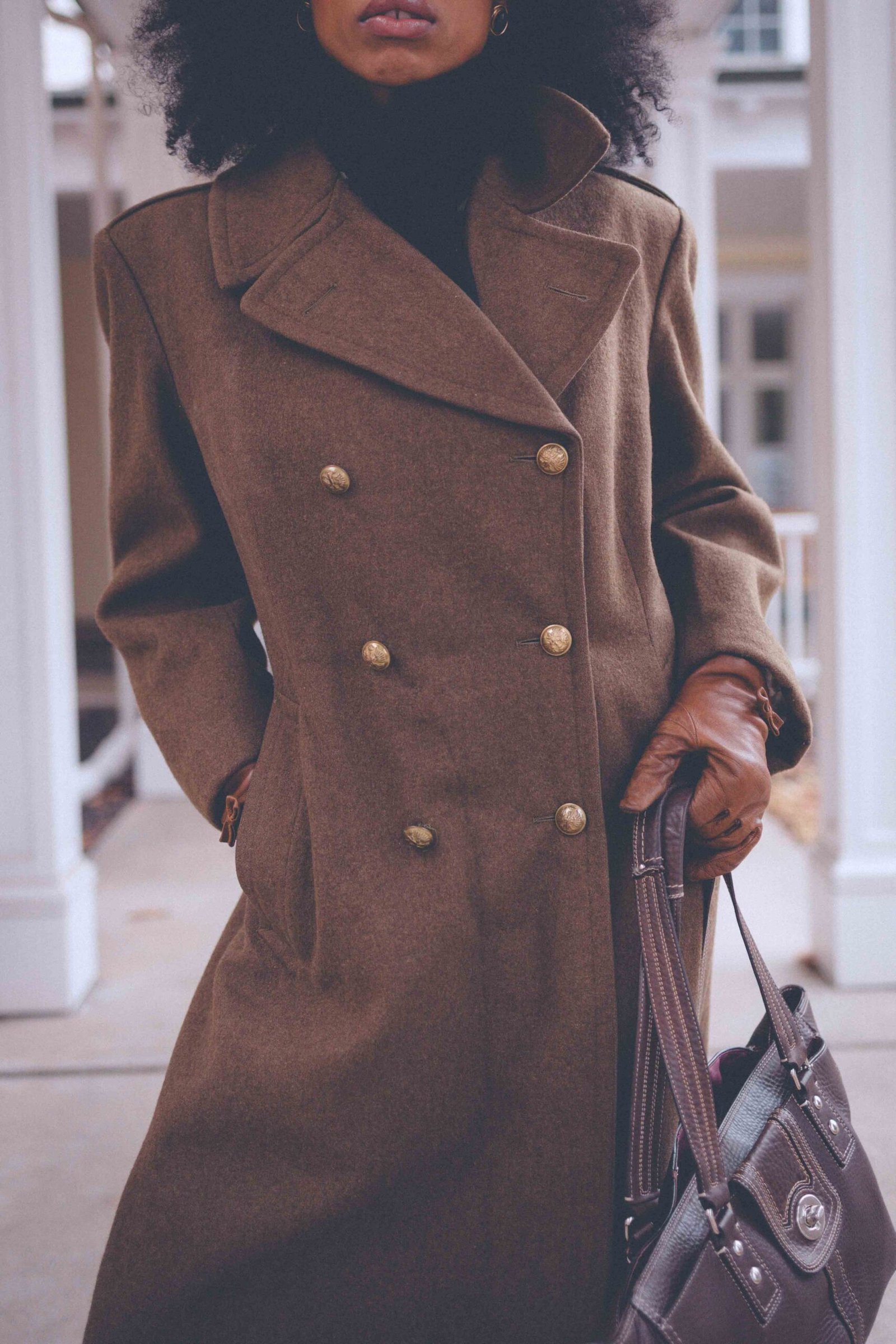 Double-breasted olive wool coat with leather gloves and a structured tote, styled as a classic winter wardrobe essential.
