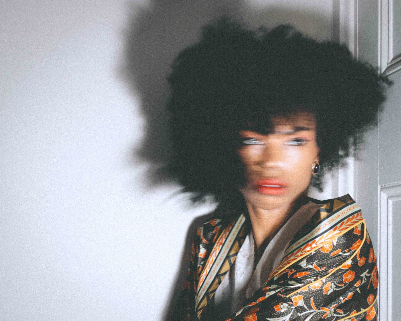 Art girl winter self-portrait with motion blur, featuring red lipstick and a patterned robe, photographed indoors during a quiet creative moment.