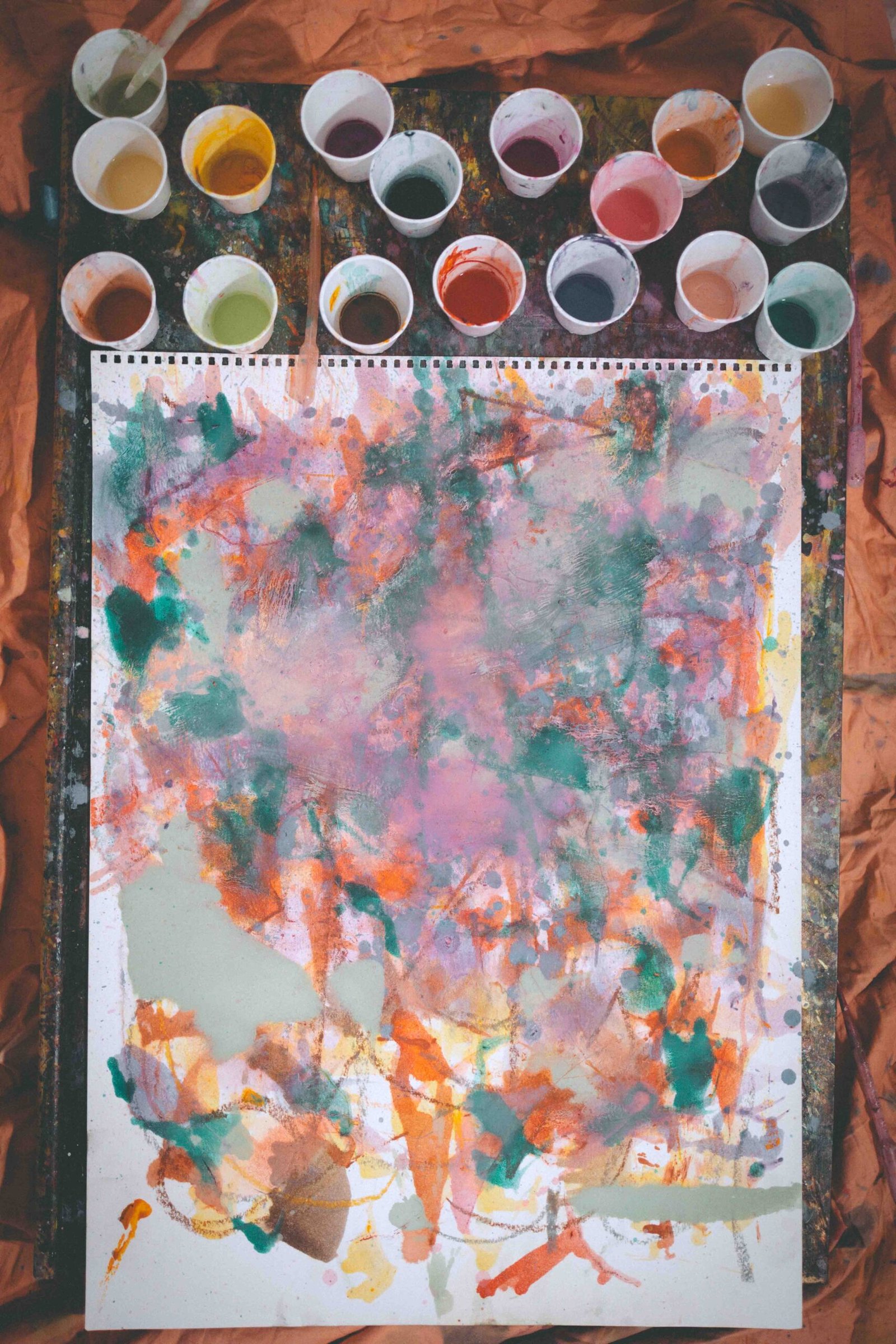 Abstract painting in progress surrounded by cups of mixed oil paint, showing painting as therapy through intuitive color and creative process.