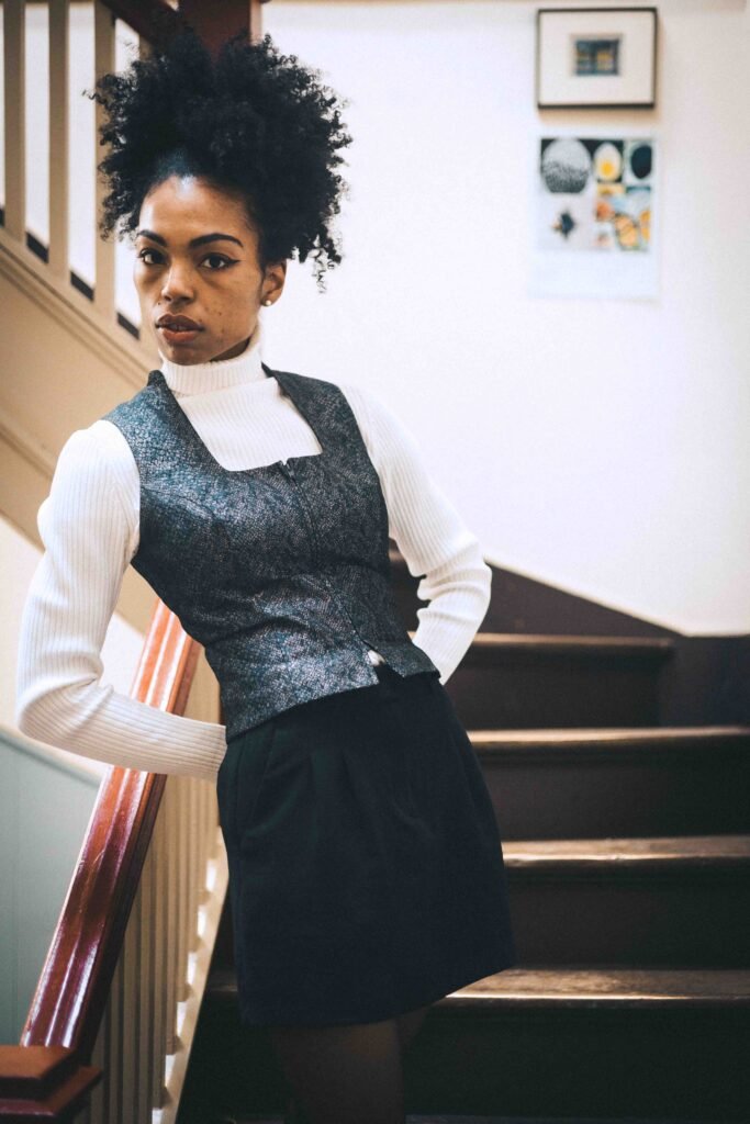 Thrifted art girl winter uniform with a vintage vest layered over a white turtleneck, styled inside a New York artist studio stairwell.
