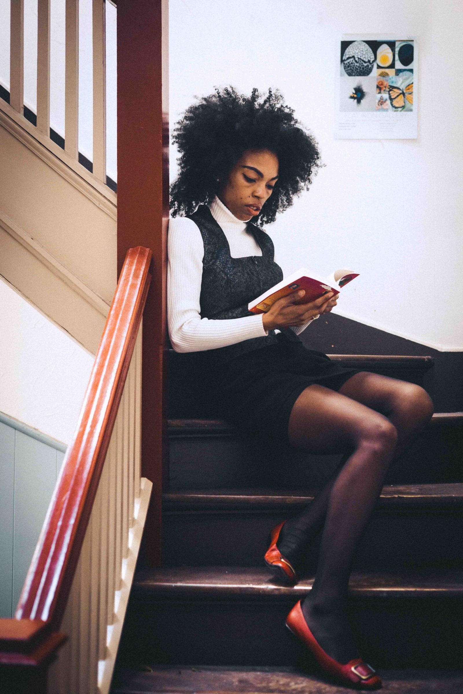 Art girl winter outfit styled with thrifted layers, sitting on stairs reading a book during a quiet creative afternoon indoors.