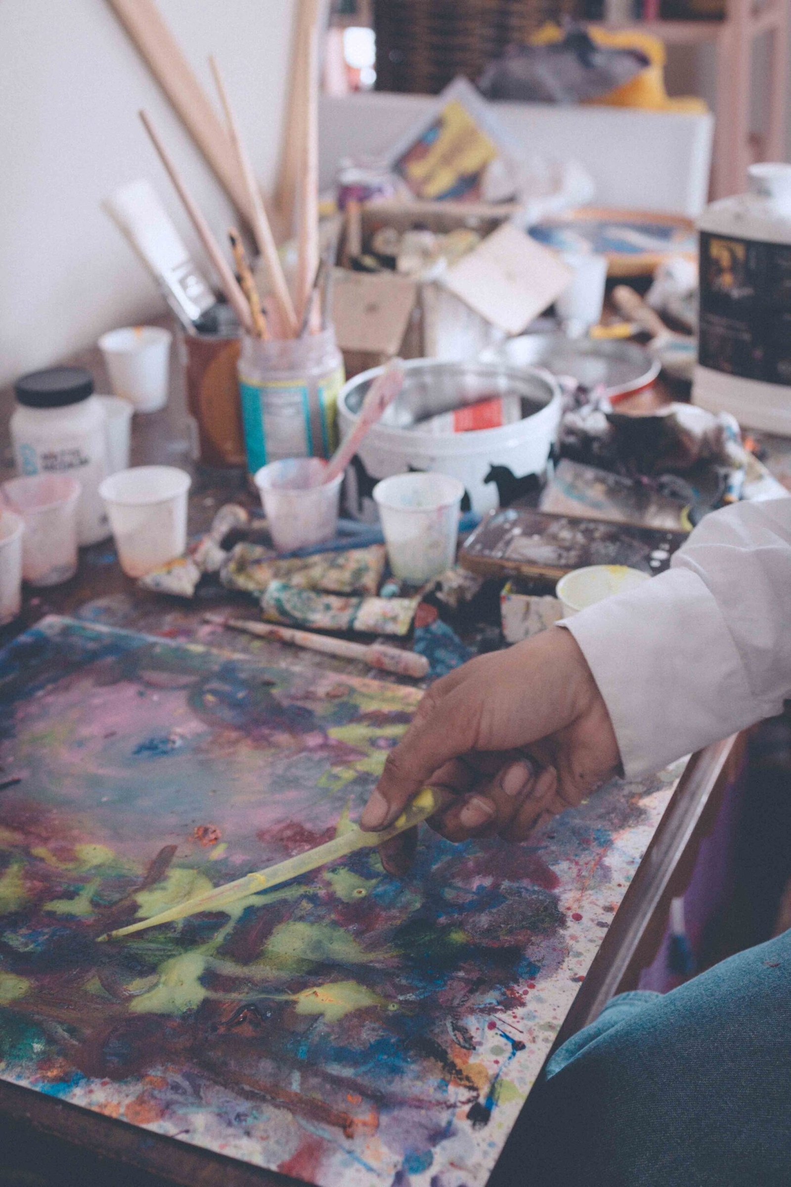 Artist painting at a studio table, using painting as therapy to process emotions through movement, color, and presence.