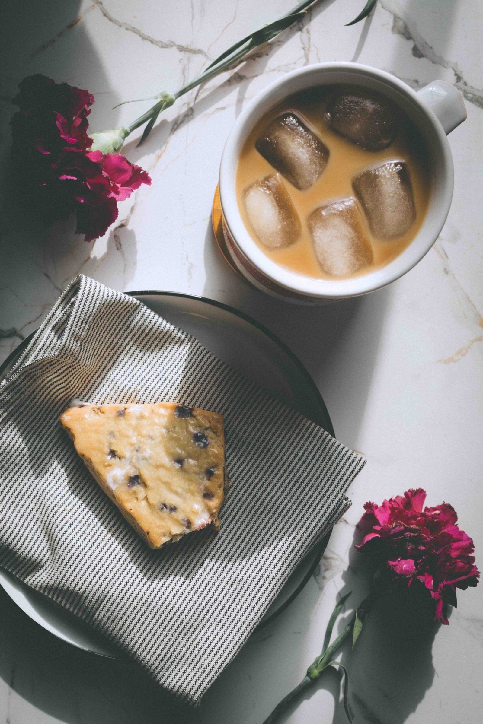 Iced coffee and a blueberry scone on a plate with flowers, a small everyday luxury enjoyed at home.
