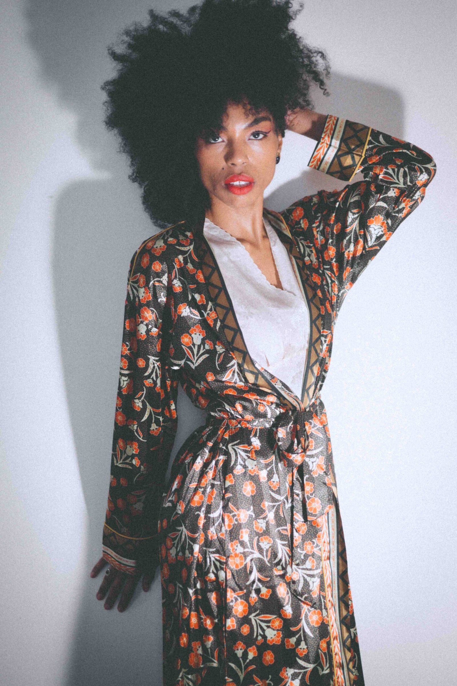 Art girl wearing a vintage floral robe styled as private glamour, soft editorial portrait with natural hair and bold red lipstick.