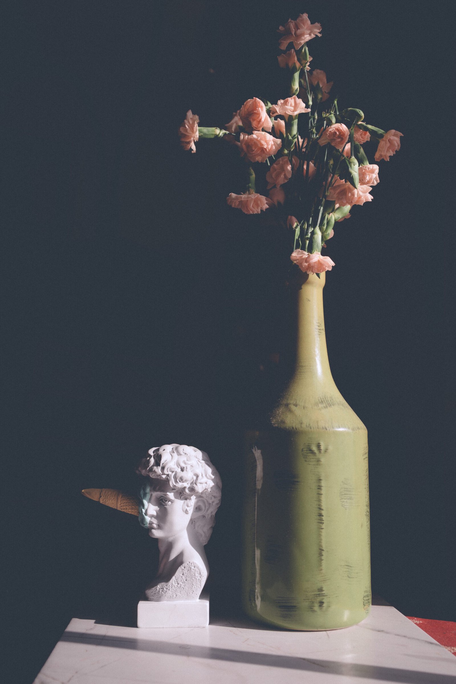 Artistic still life featuring pink carnations and a sculptural bust, inspired by chiaroscuro and themes of self love on Valentine’s Day.