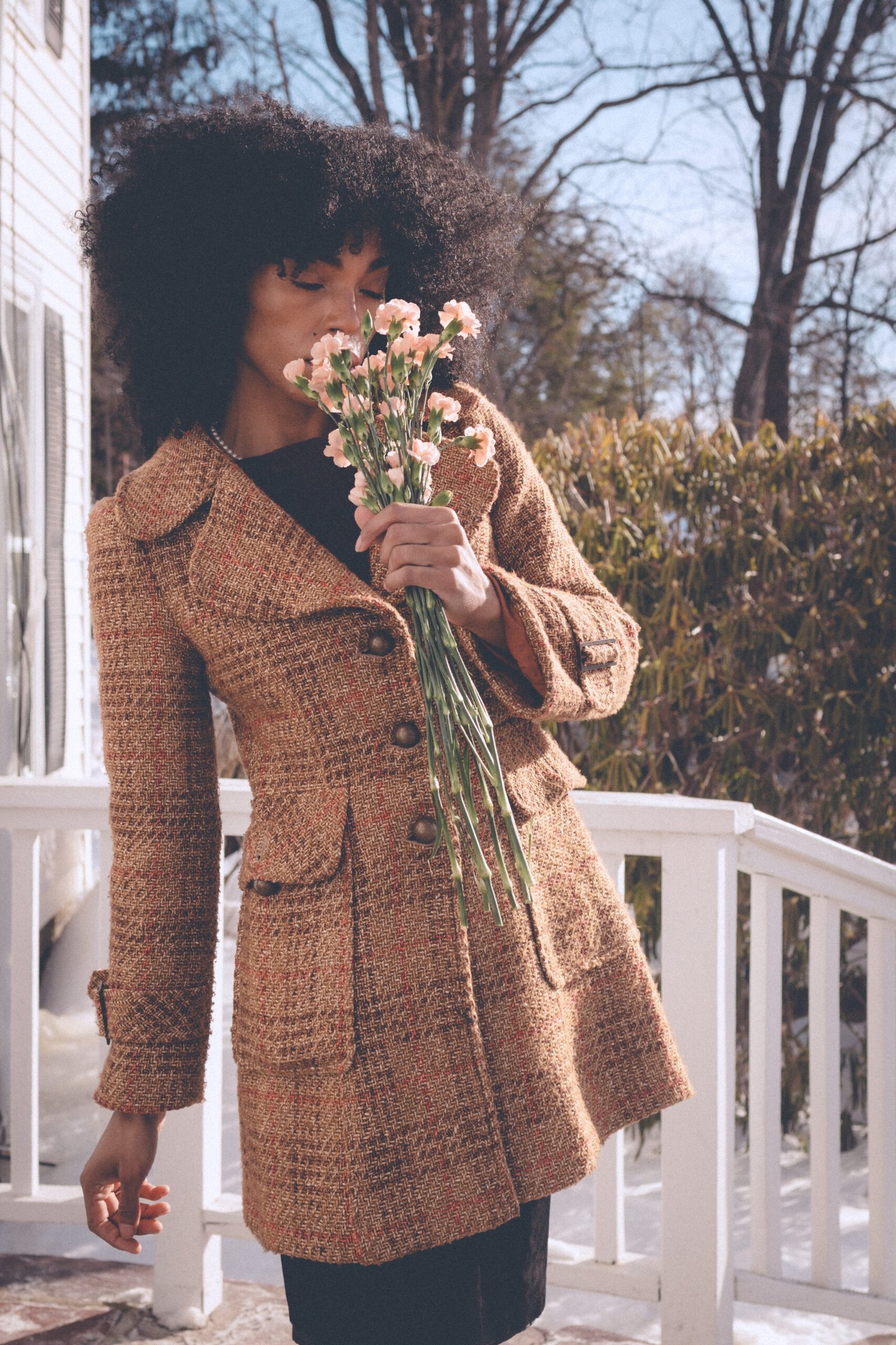 Woman wearing a vintage tweed coat holding pink carnations on Valentine’s Day, reflecting on being single and practicing self love.