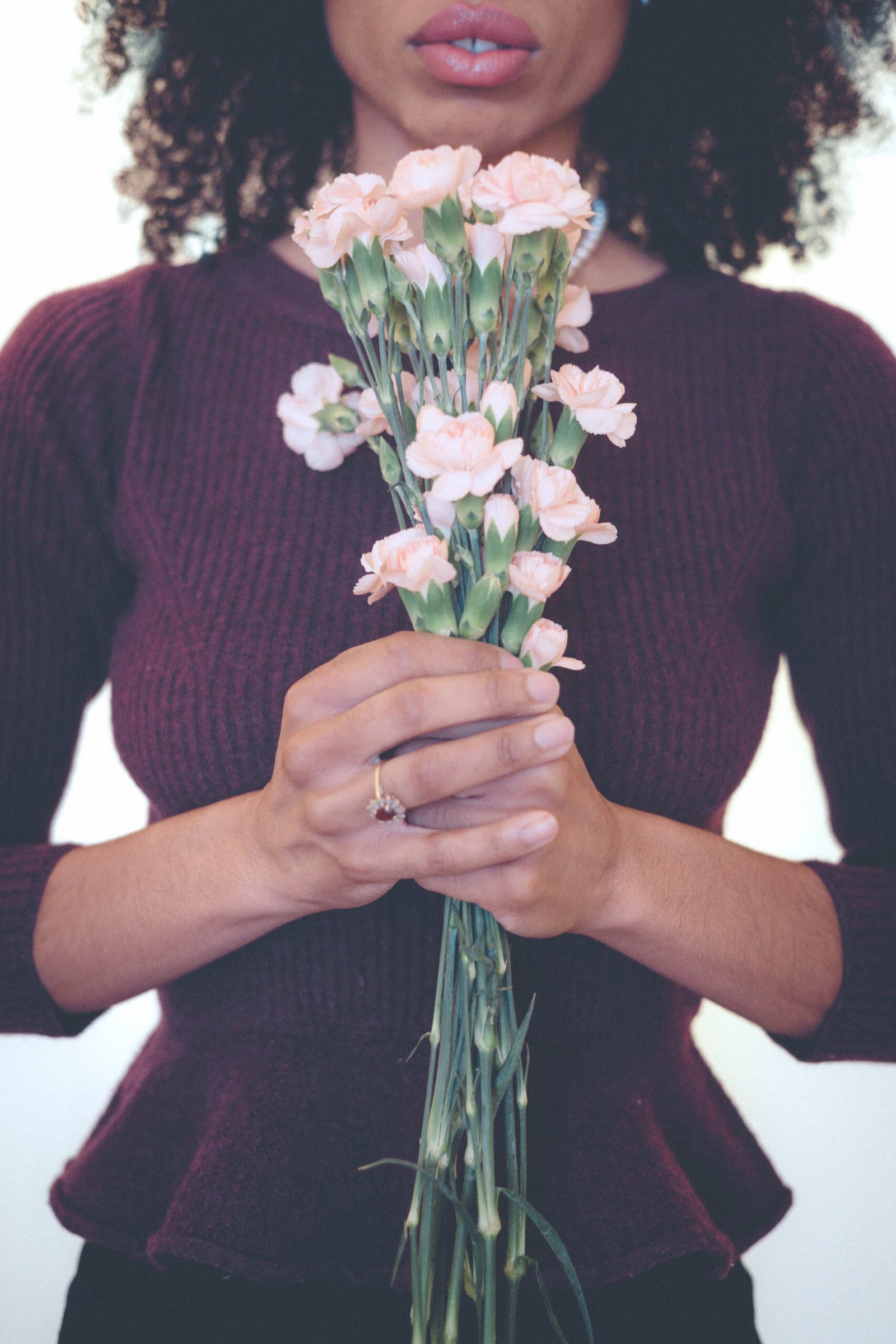 Woman holding pink carnations close to her chest on Valentine’s Day, symbolizing self love and tenderness while single.