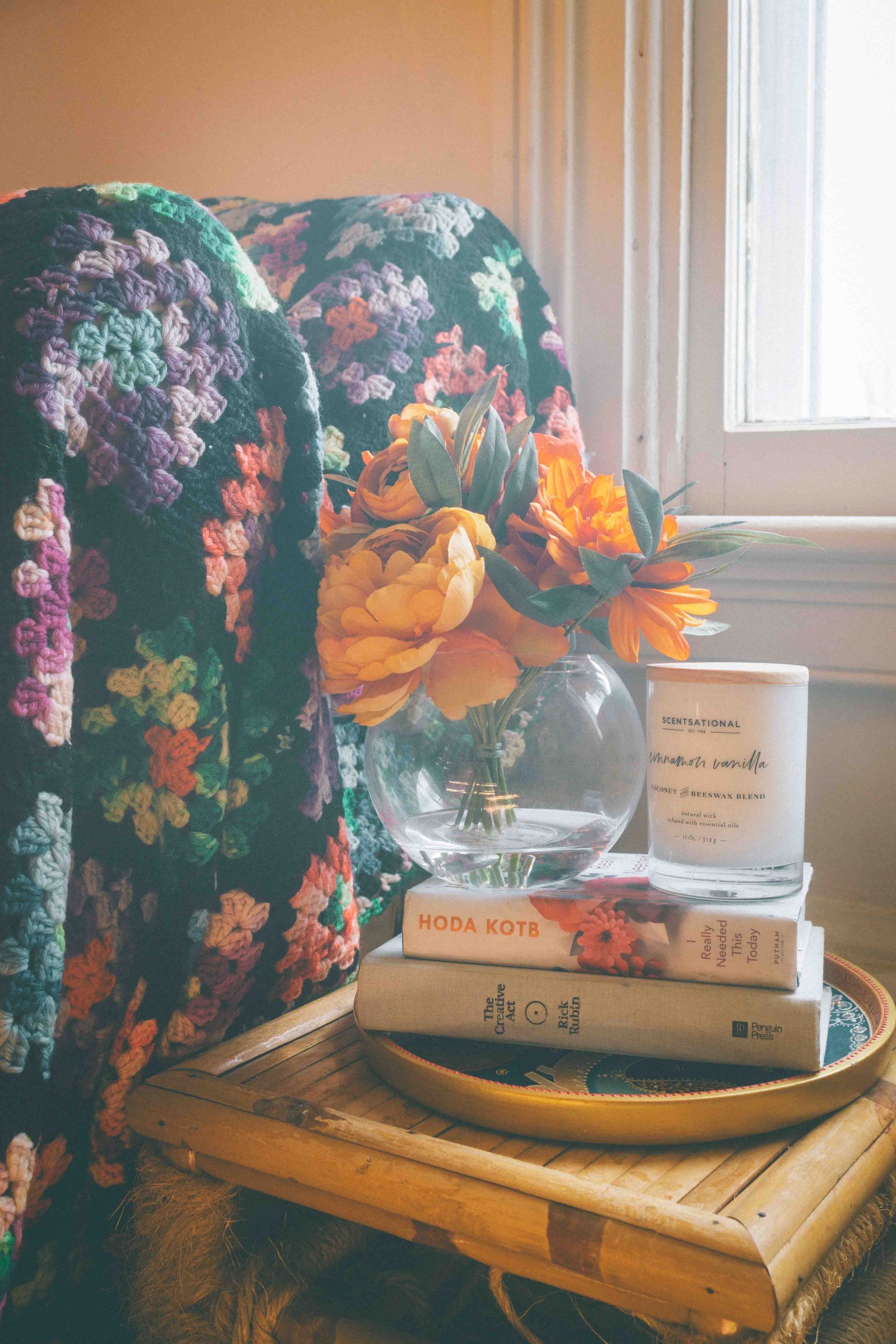 Cozy bohemian apartment detail shot of floral print throw pillow and styled vignette of flowers, candle, and stacked books. 