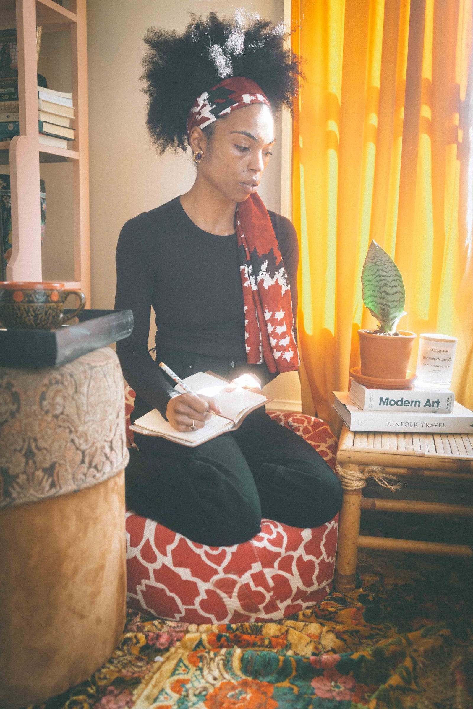 Woman journaling in a cozy bohemian apartment with warm light, layered textiles, and thrifted decor