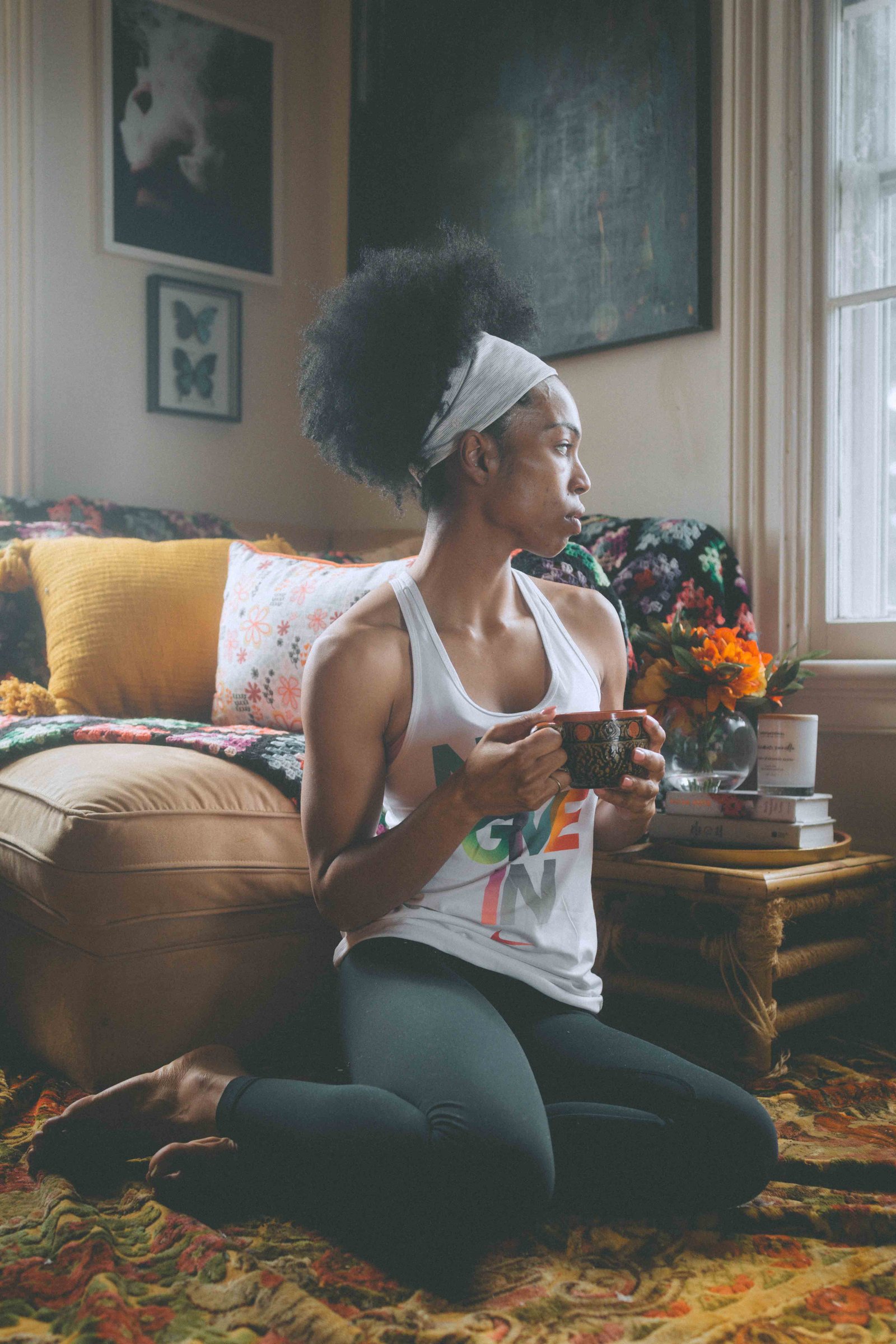 Woman sitting on the floor with coffee in a cozy bohemian apartment with layered textiles and warm natural light