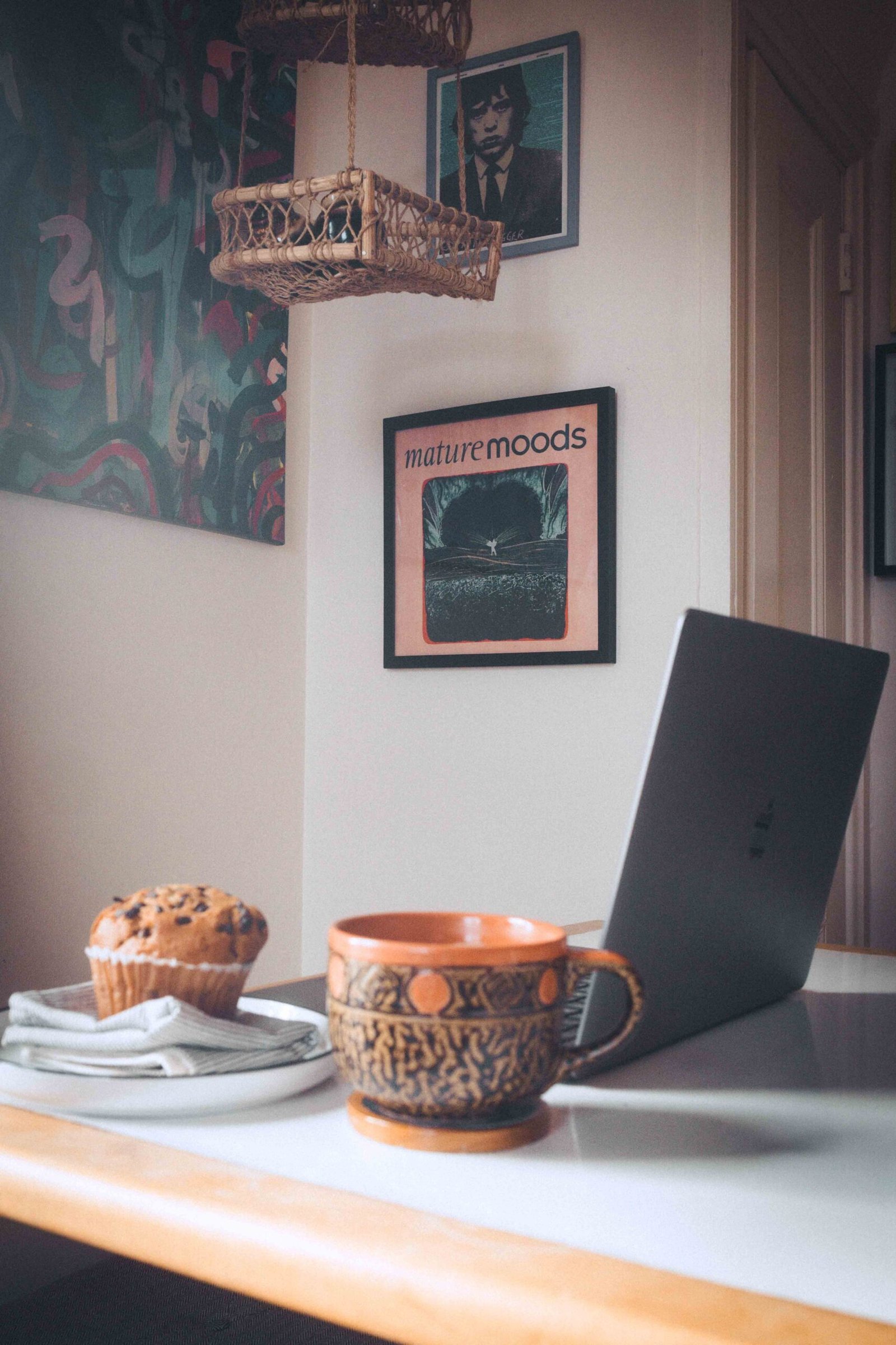 Cozy bohemian apartment desk setup with coffee mug, laptop, and breakfast in soft natural light