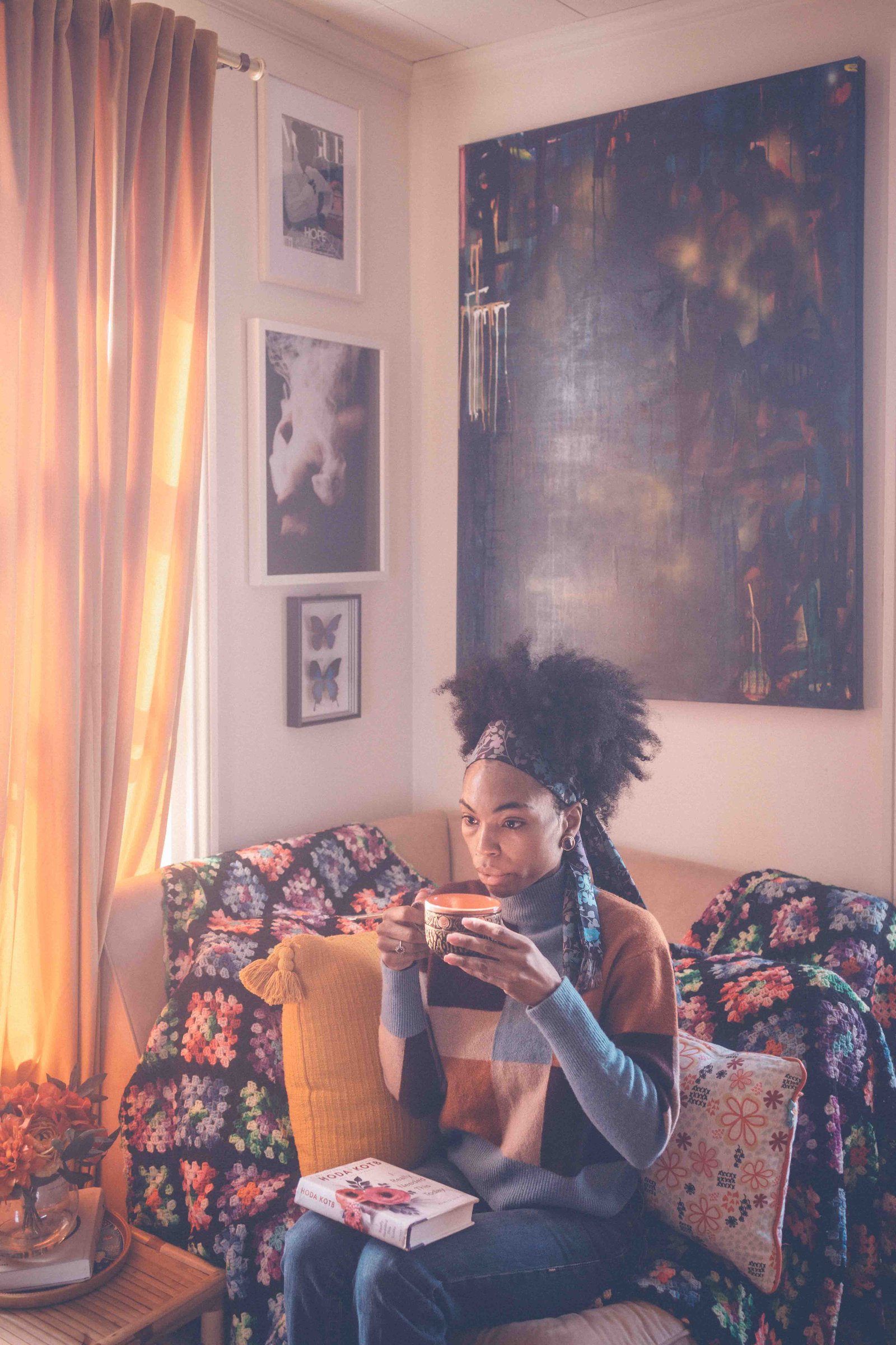 Woman relaxing in a cozy bohemian apartment reading corner with layered textiles and art gallery wall