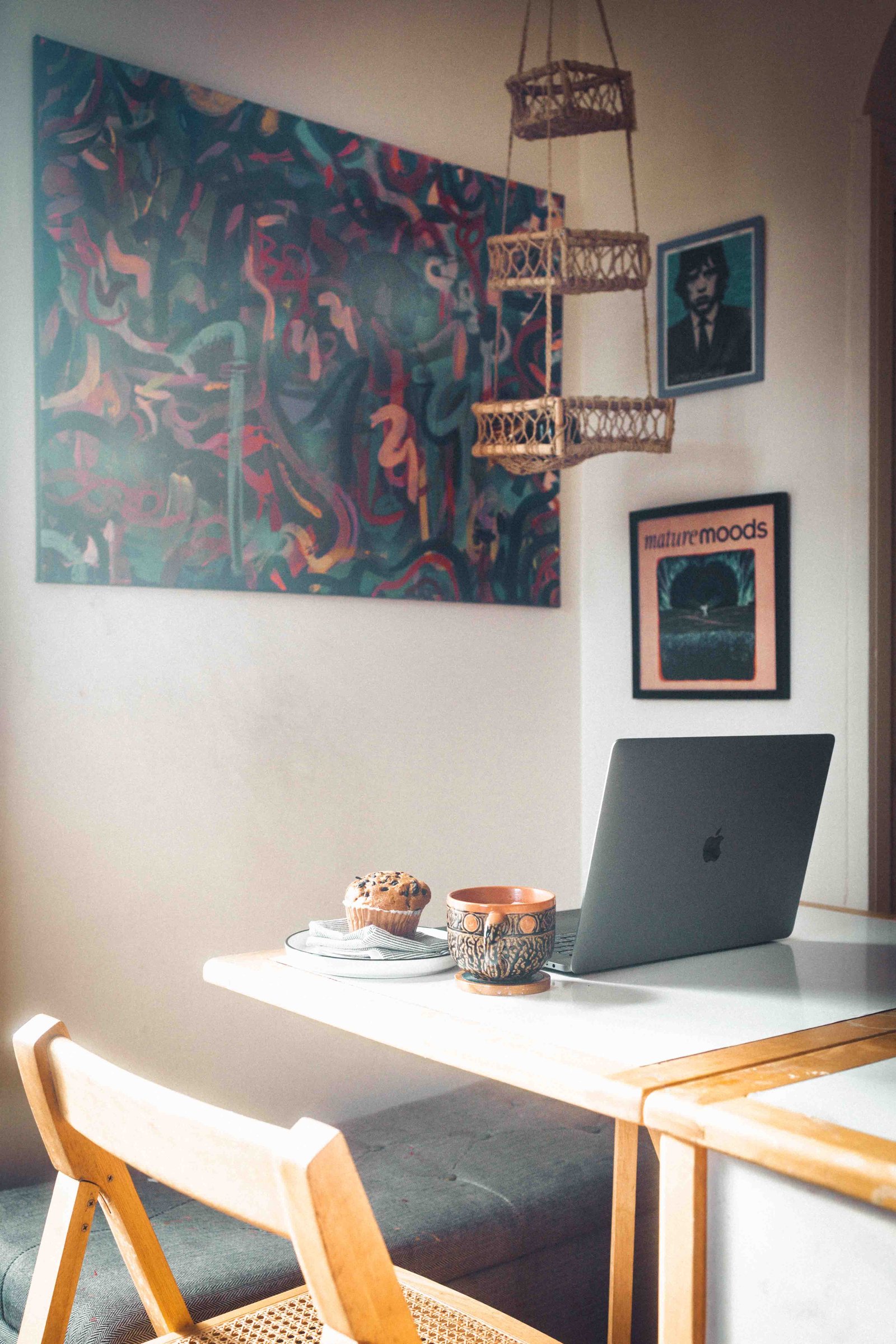 Bohemian apartment workspace with wooden desk, laptop, coffee mug, and muffin under warm natural light
